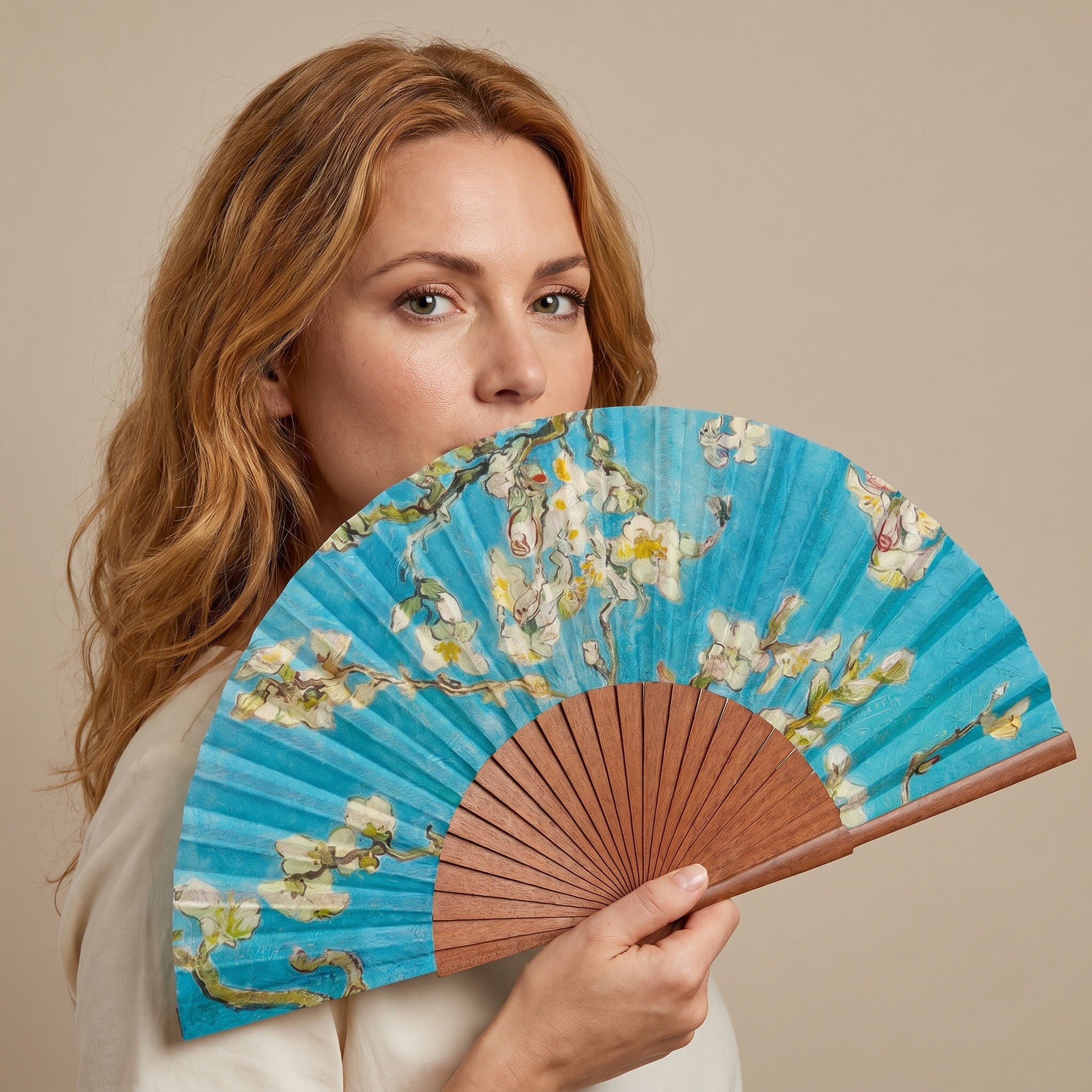 A woman holding the Van Gogh Print Hand Fan Delphine, with its Van Gogh Almond Blossom print on light blue, against a soft neutral background.