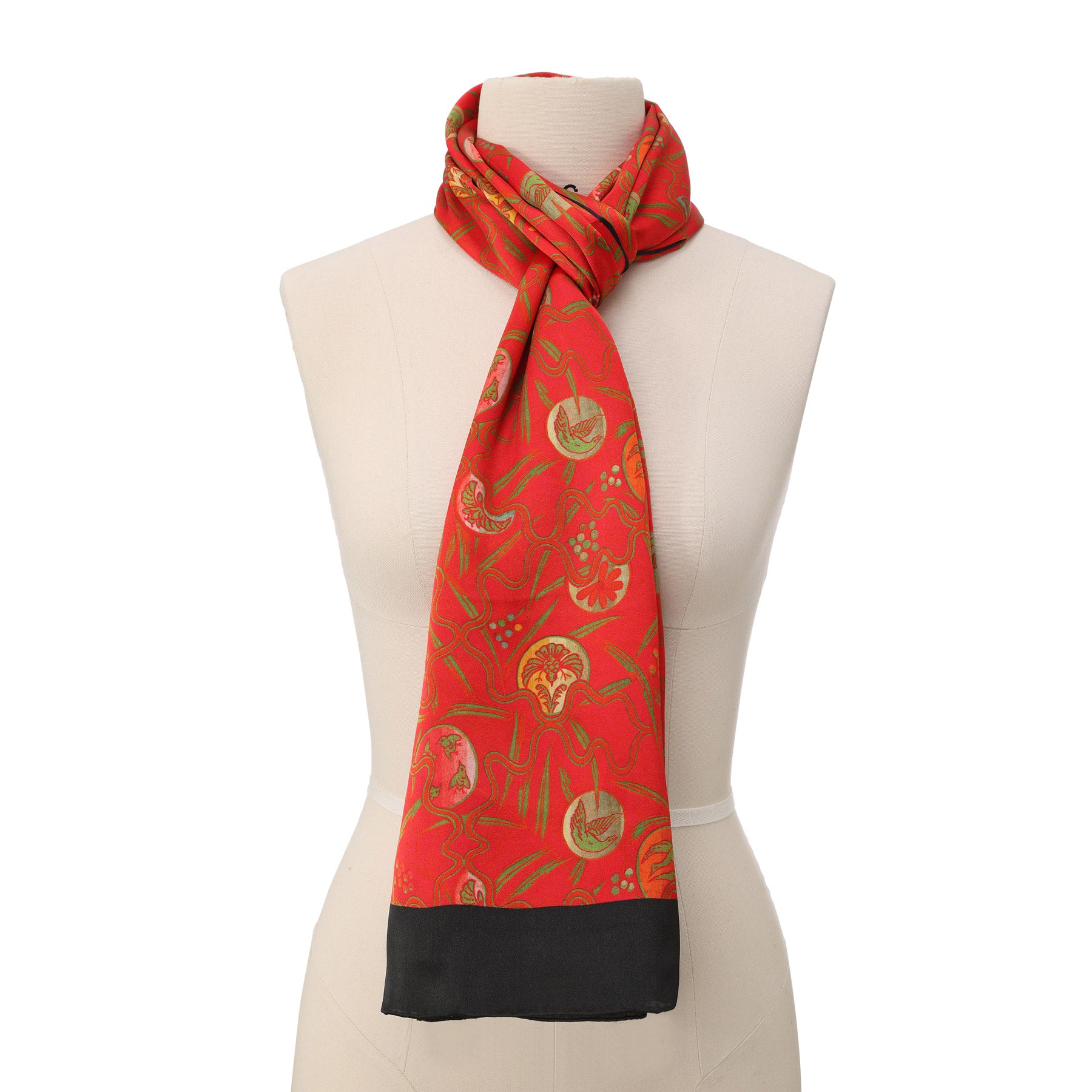 A close-up of the Red Silk Scarf with Abstract Floral Print Kabuki, showing red and black fabric with gold and green patterns, detailed with a black trim along the edge, draped in soft folds.