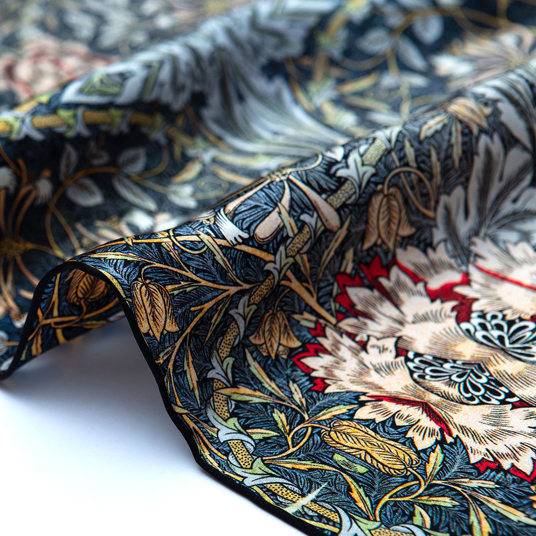 A close-up of the Grey Silk Scarf Erna, showcasing intricate floral and leaf patterns in dark blue, gold, red, and cream on soft folded silk with a beautiful sheen.