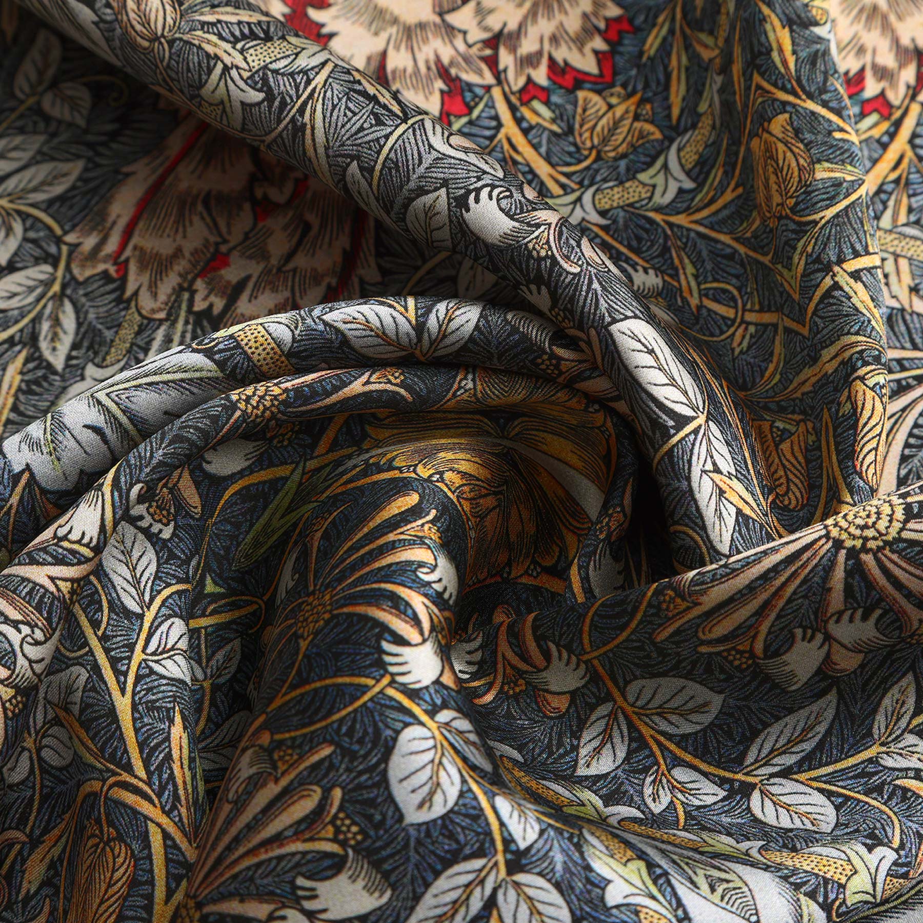 A close-up of the Grey Silk Scarf Erna, showcasing intricate floral and leaf patterns in dark blue, gold, red, and cream on soft folded silk with a beautiful sheen.