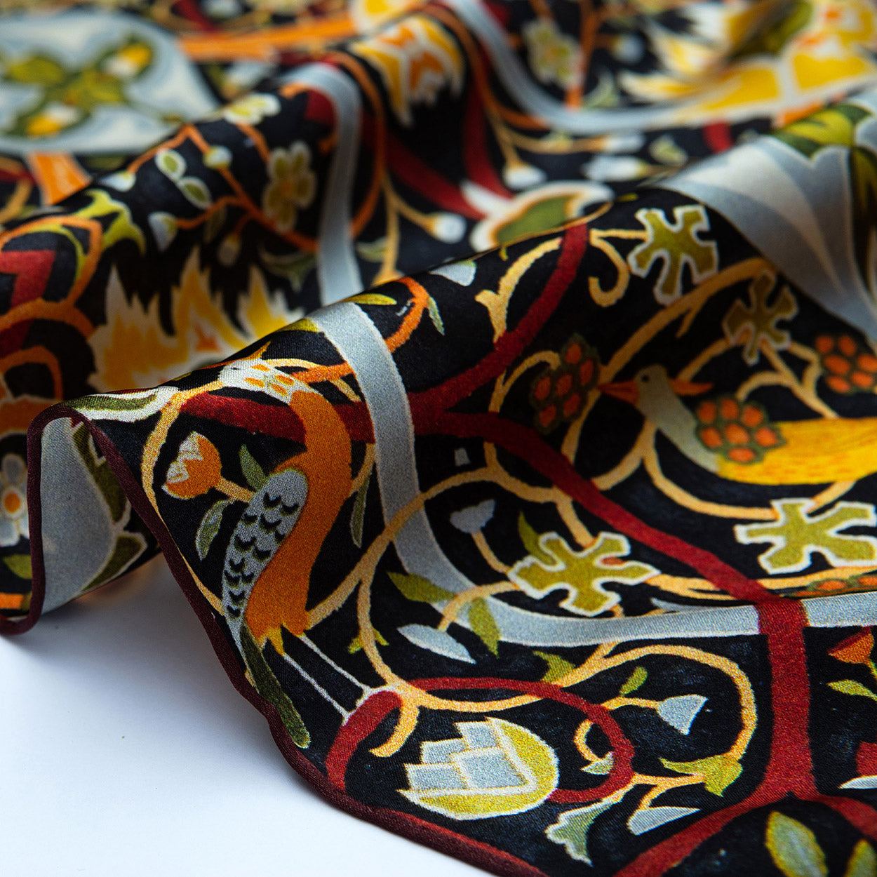 A close-up of the Vintage Floral Silk Scarf with Ornate Bird & Bloom Motifs, featuring vivid yellow, orange, green, black, and red stylized birds, leaves, and flowers in a nature-inspired pattern. The natural silk is softly draped.