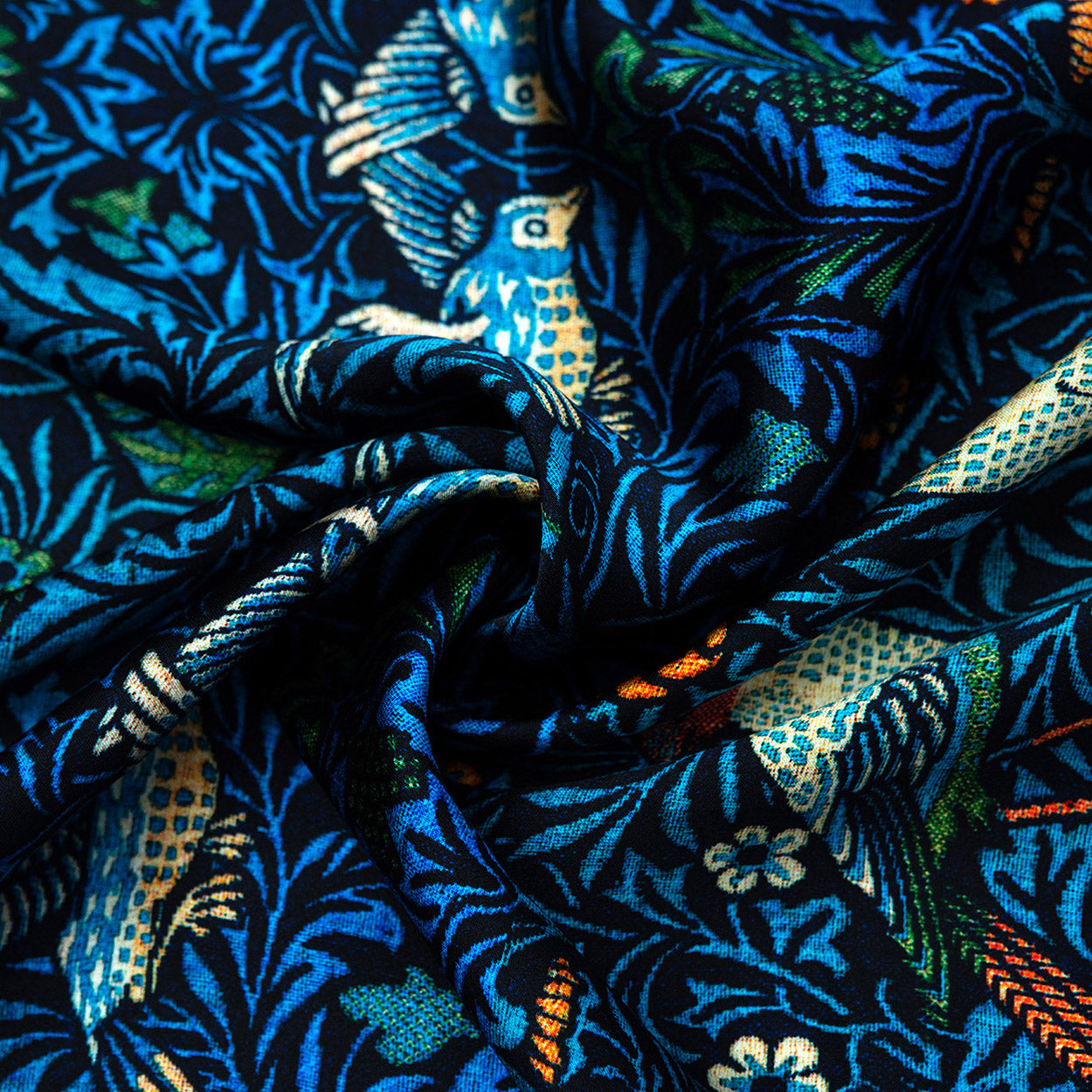 The William Morris Inspired Silk Scarf features intricate bird and floral motifs in blue, green, yellow, and orange, gathered in soft folds for a textured effect reminiscent of Victorian Arts & Crafts design.