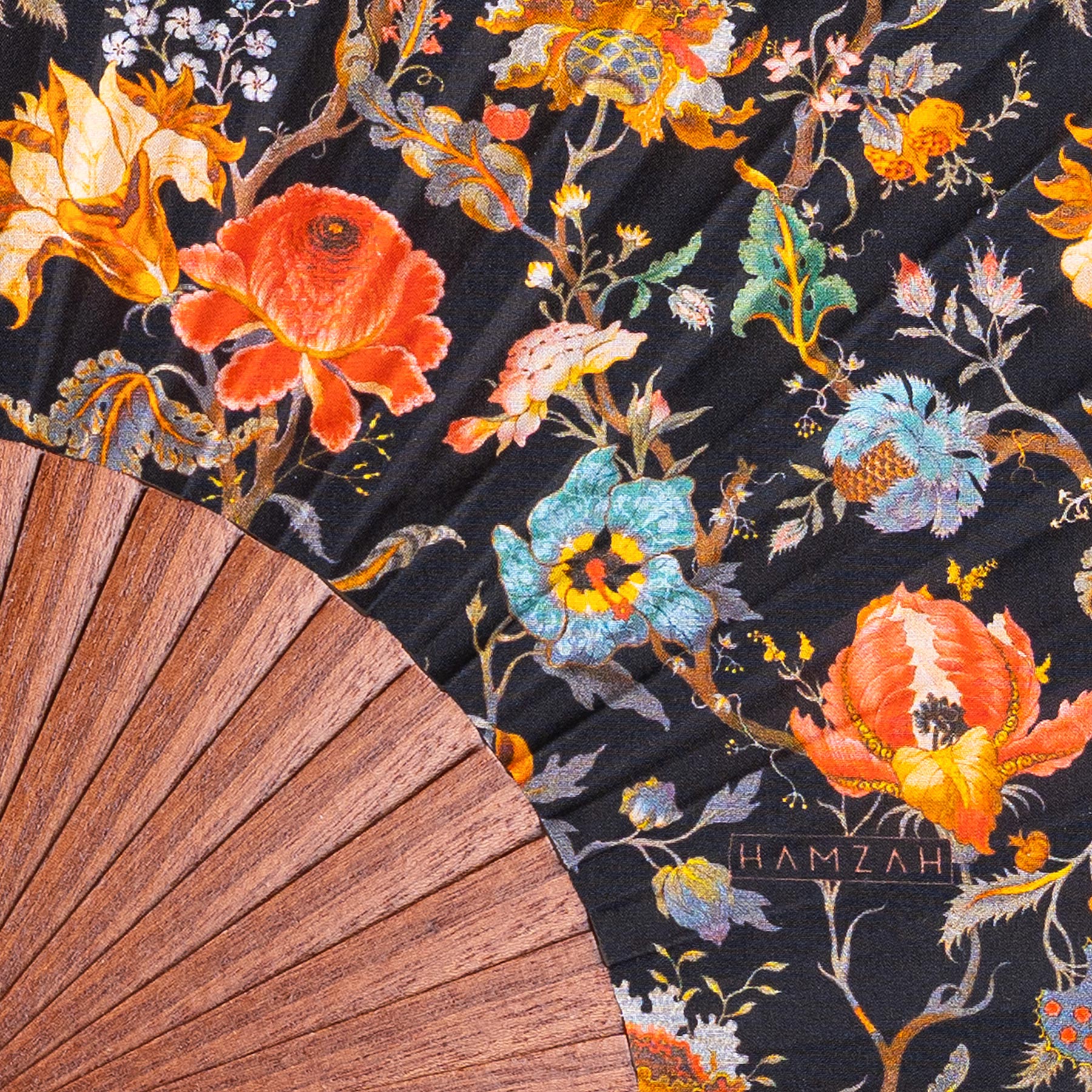 The William Morris Print Hand Fan Aubrey features vibrant red, yellow, orange, blue, and green floral patterns on black silk fabric with a wooden base and the word HAMZAH visible on the fabric.