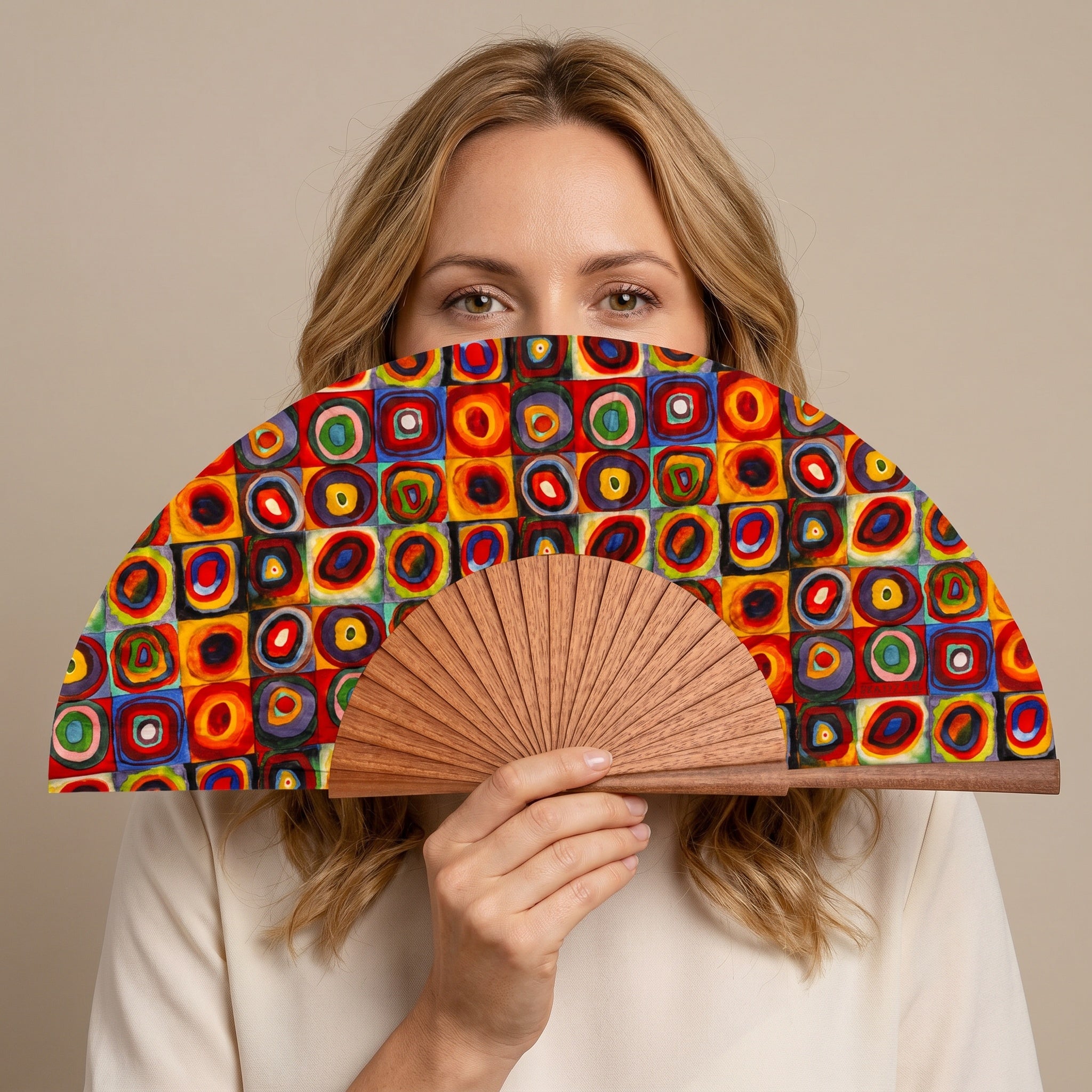 A woman in a summer outfit holding the open Kandinsky Print Hand Fan Lorelei with its Kandinsky concentric circles colourful print.