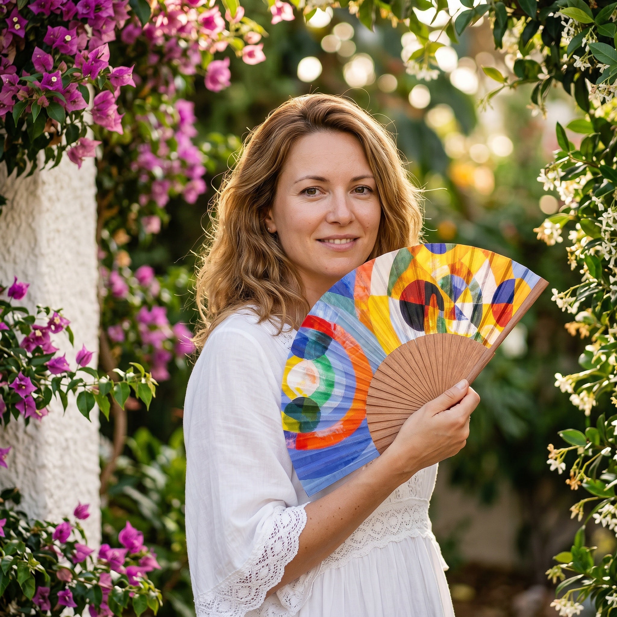 A woman in a summer outfit holding the open Robert Delaunay Print Hand Fan Elise with its Robert Delaunay circular forms colourful print.