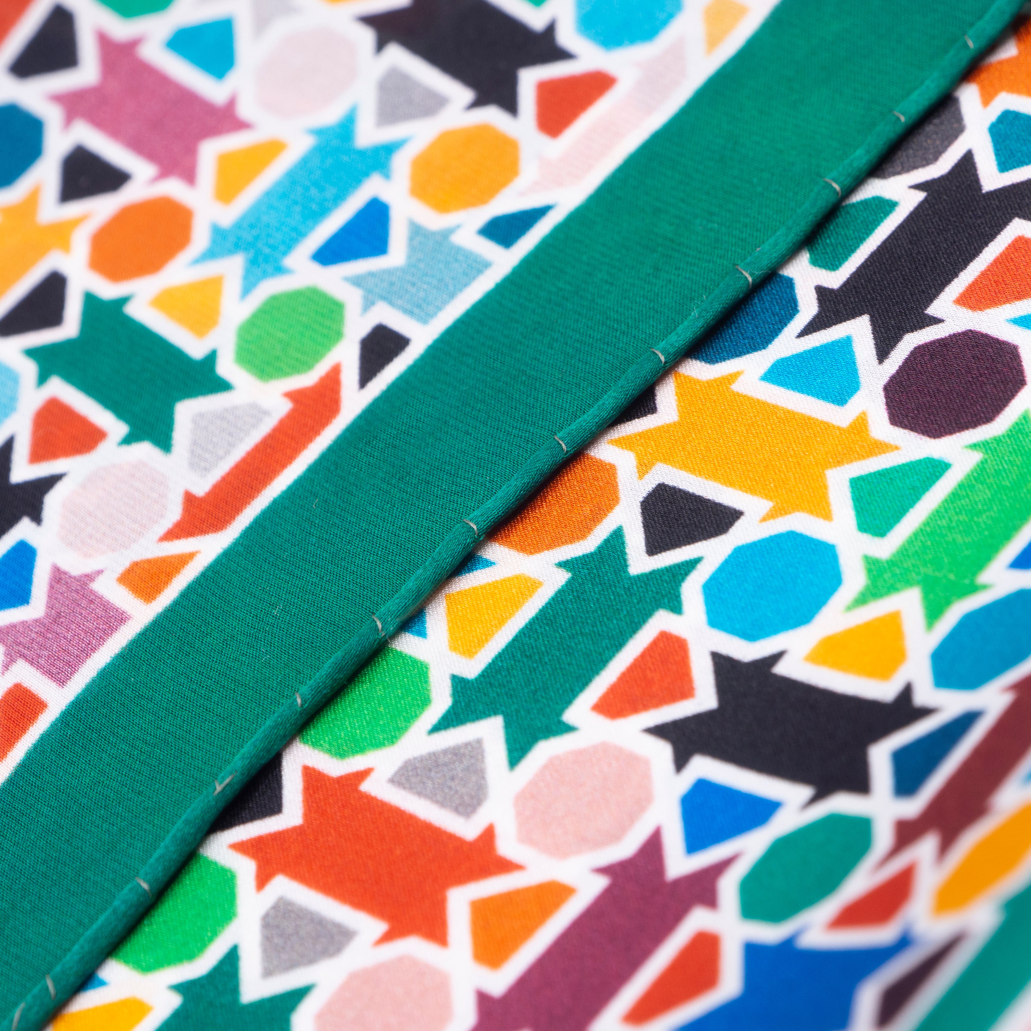 Close-up of the Multicolor Silk Square Scarf Amal in silk, showcasing a vibrant geometric pattern with arrows, circles, and hexagons, split diagonally by a solid green stripe and finished with hand rolled hems.