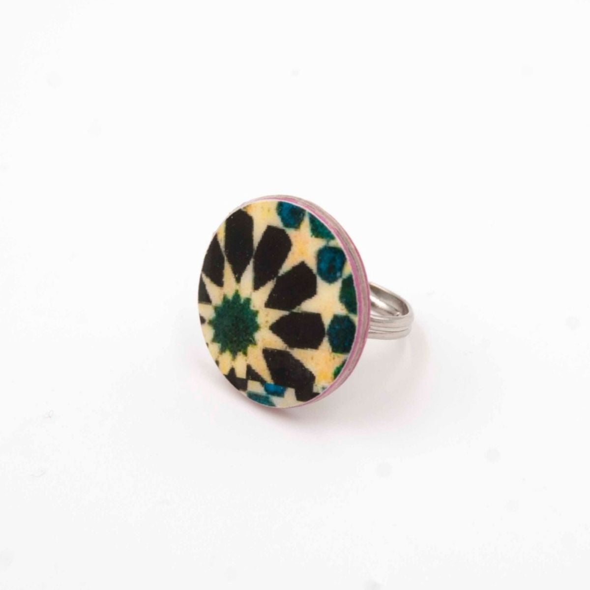The Moroccan Tiles Inspired Ring Jabugo by Azul Añil is a silver ring featuring a multicolored mosaic of black, yellow, and green geometric shapes resembling a starburst. Handmade to highlight its artistic detail, it sits on a white background.