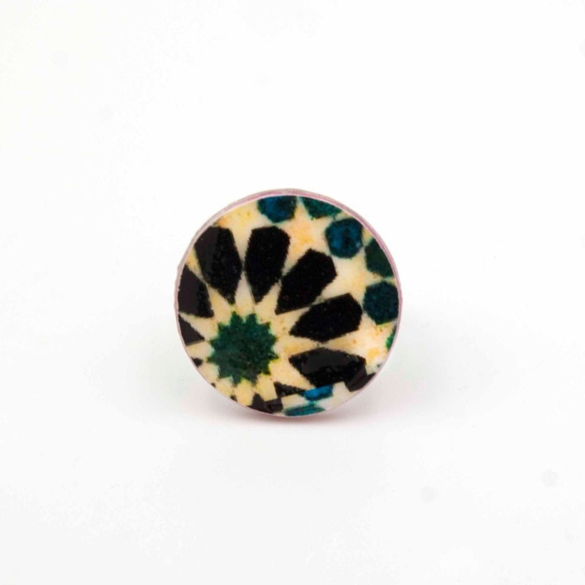 The Moroccan Tiles Inspired Ring Jabugo by Azul Añil is a round ceramic piece featuring a geometric design with black, blue, and green shapes on a white background, resembling a radial kaleidoscope pattern similar to intricate Moroccan tiles.