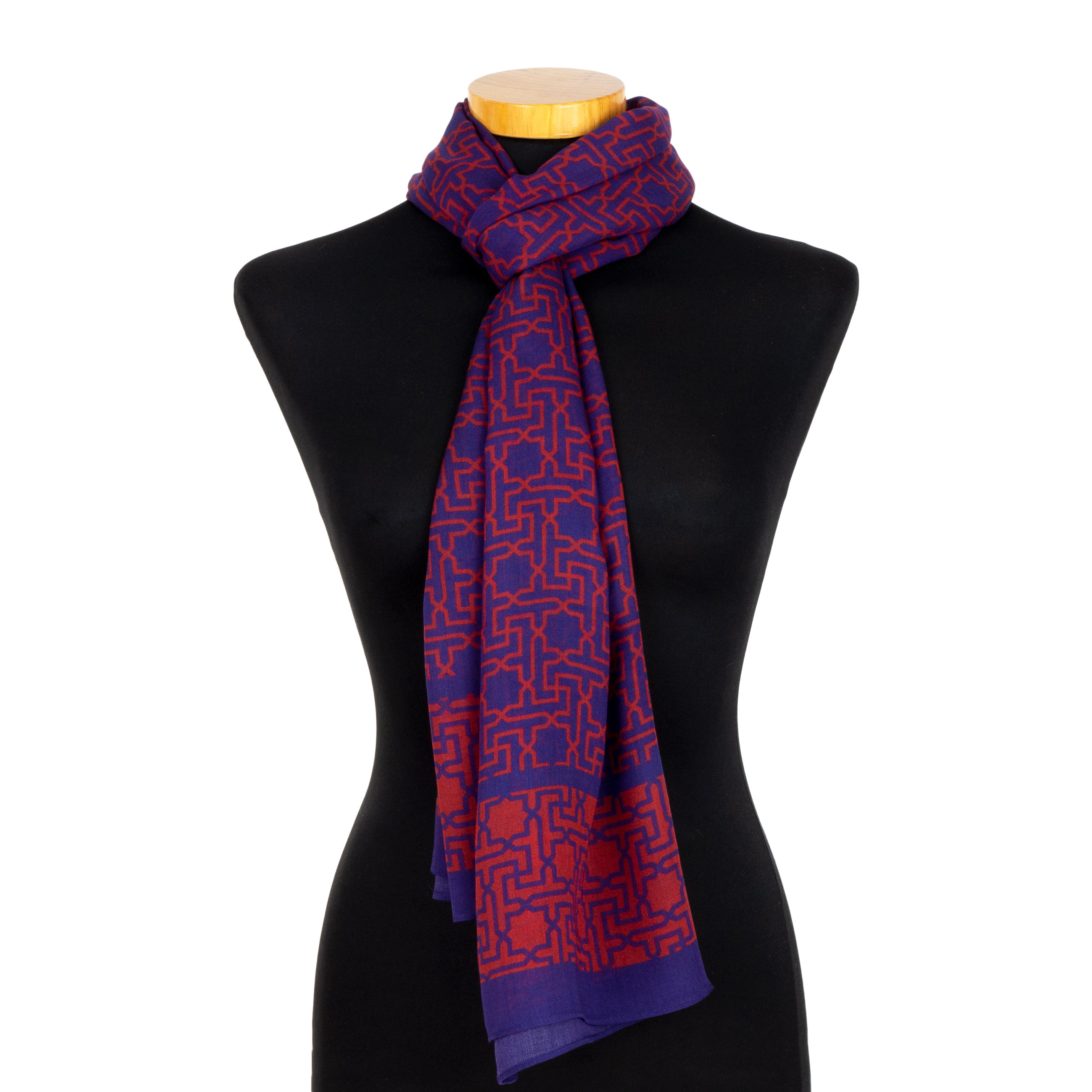 A blue and red scarf, Rawda v2, featuring Alhambra-inspired motifs and designed in Spain, is draped around the neck of a black dress form mannequin with a wooden stand.