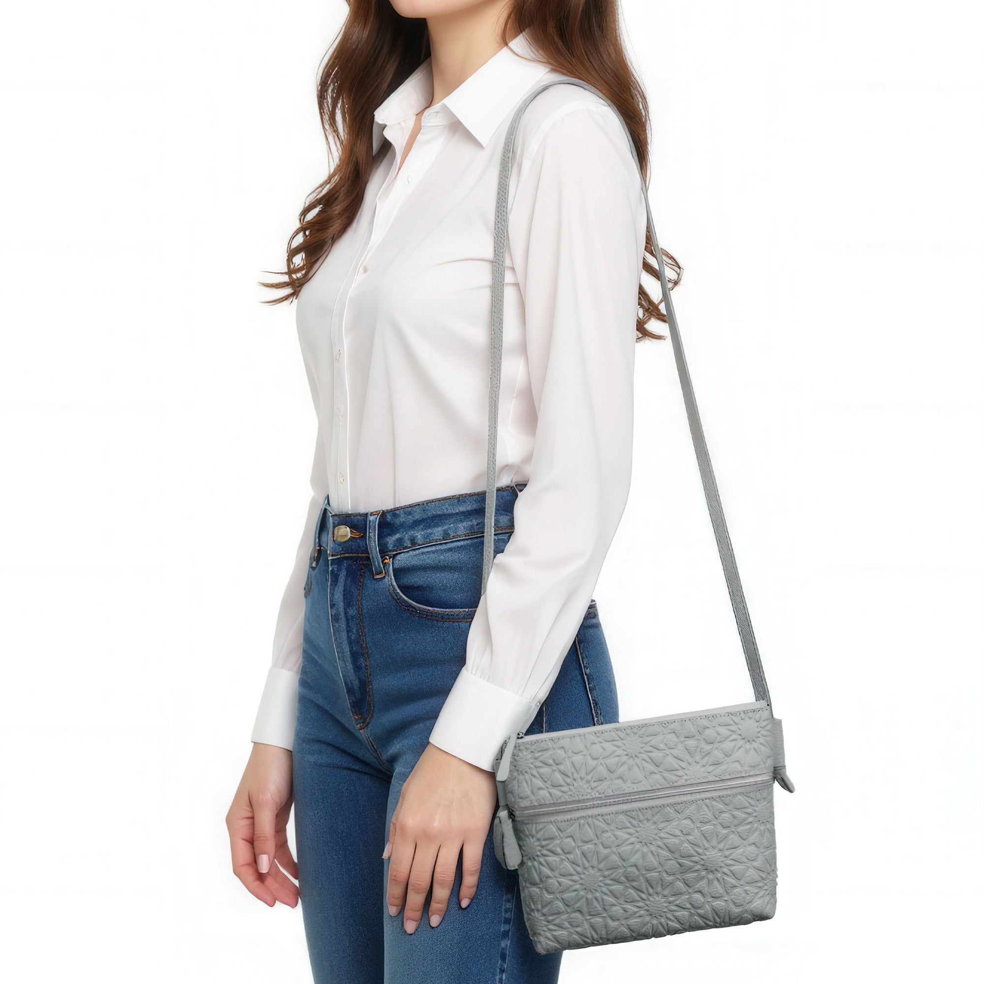 A woman in a white button-up shirt and blue jeans is shown from the shoulders down, carrying the Gray Embossed Crossbody Bag with Islamic Design Pattern (Copia) over her shoulder.