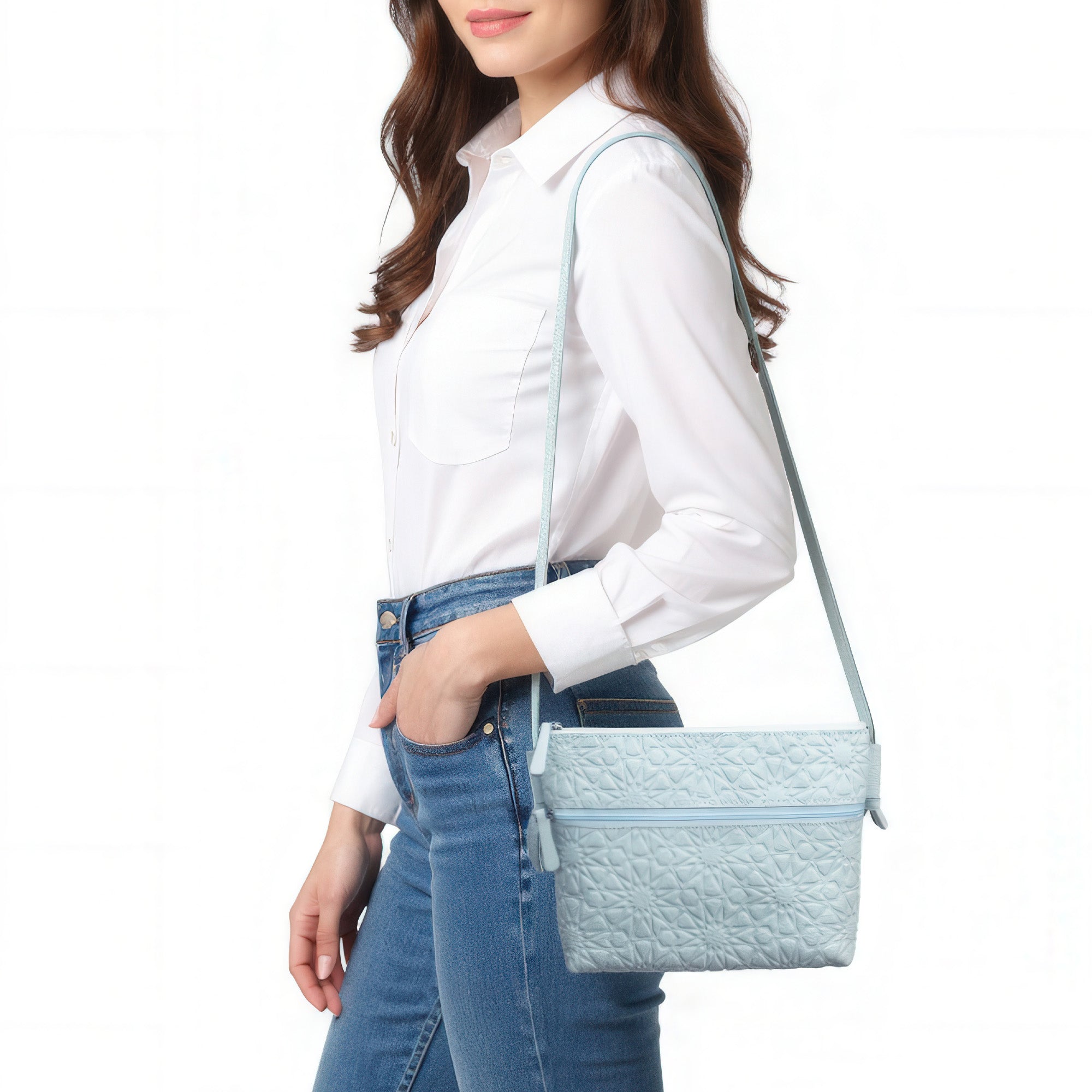 A woman in a white long-sleeve shirt and blue jeans carries a Light Blue Embossed Crossbody Bag with an Islamic design pattern over her shoulder against a white background.