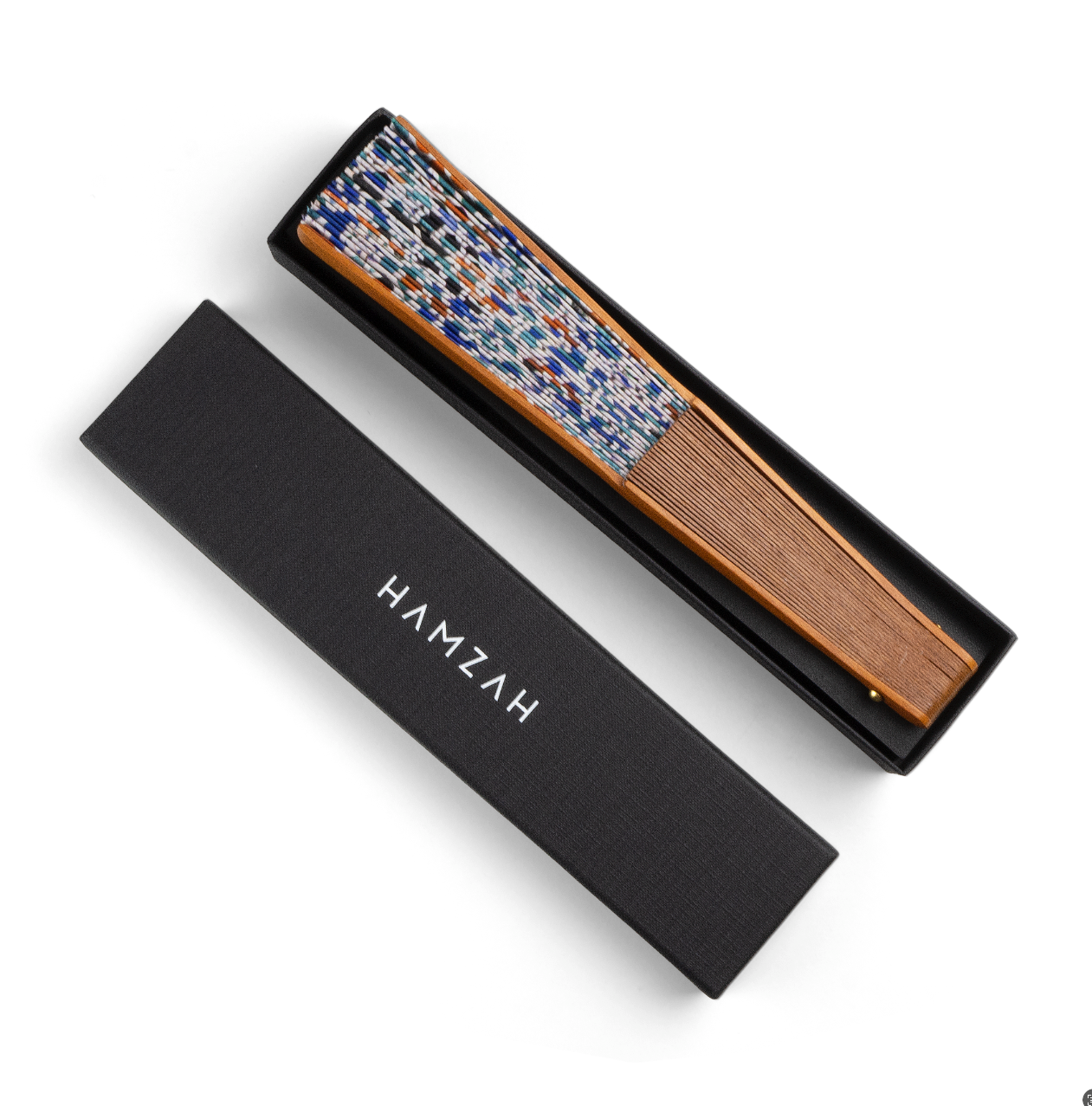 The Silk & Wood fan Balat features handcrafted wooden slats and a colorful edge inspired by Andalusian Islamic geometry. It comes folded inside a black box with HAMZAH in white on the side-positioned lid.