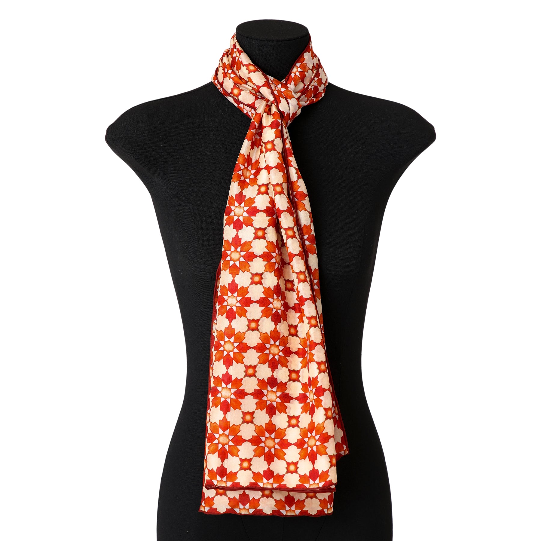 A mannequin displays the Orange Silk Scarf with Islamic Print Cosmo, crafted from watercolor silk and featuring a vibrant orange pattern. The scarf is neatly draped and knotted at the chest for an elegant look.