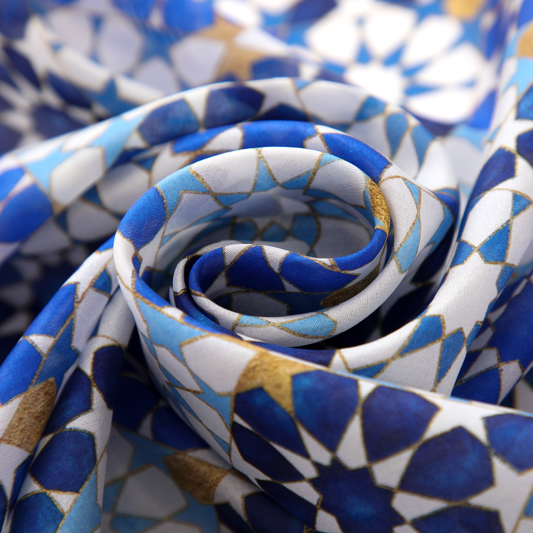 Close-up of the Blue Silk Scarf with Islamic Pattern DalAhorra, featuring interlocking blue, white, and gold shapes inspired by Andalusian designs—artistically folded to highlight its elegant silk fabric.