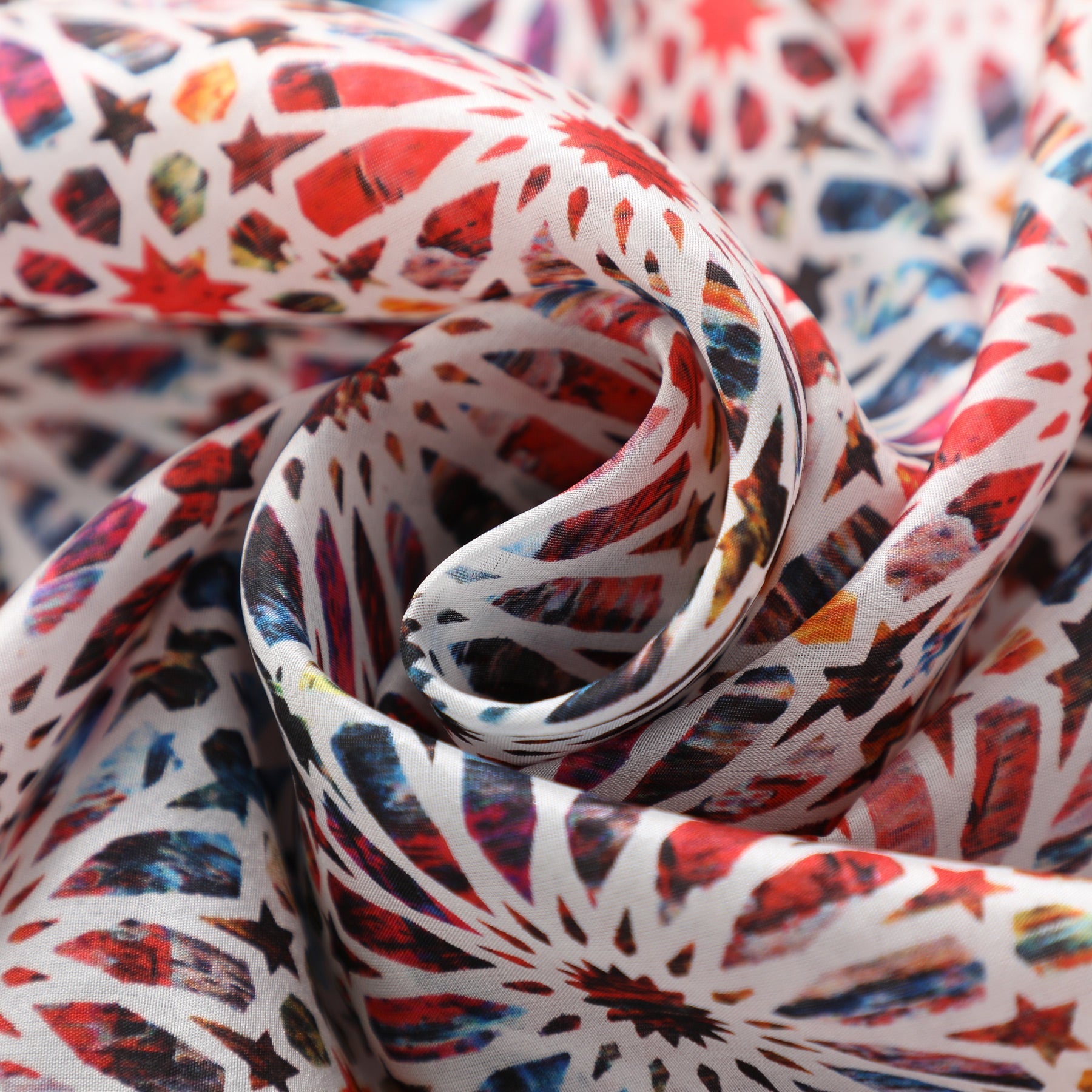A close-up of the Multicolor Silk Scarf Sakina, showcasing smooth, lightweight silk with colorful geometric patterns inspired by Islamic art and red, blue, and black starburst designs gently spiraled.