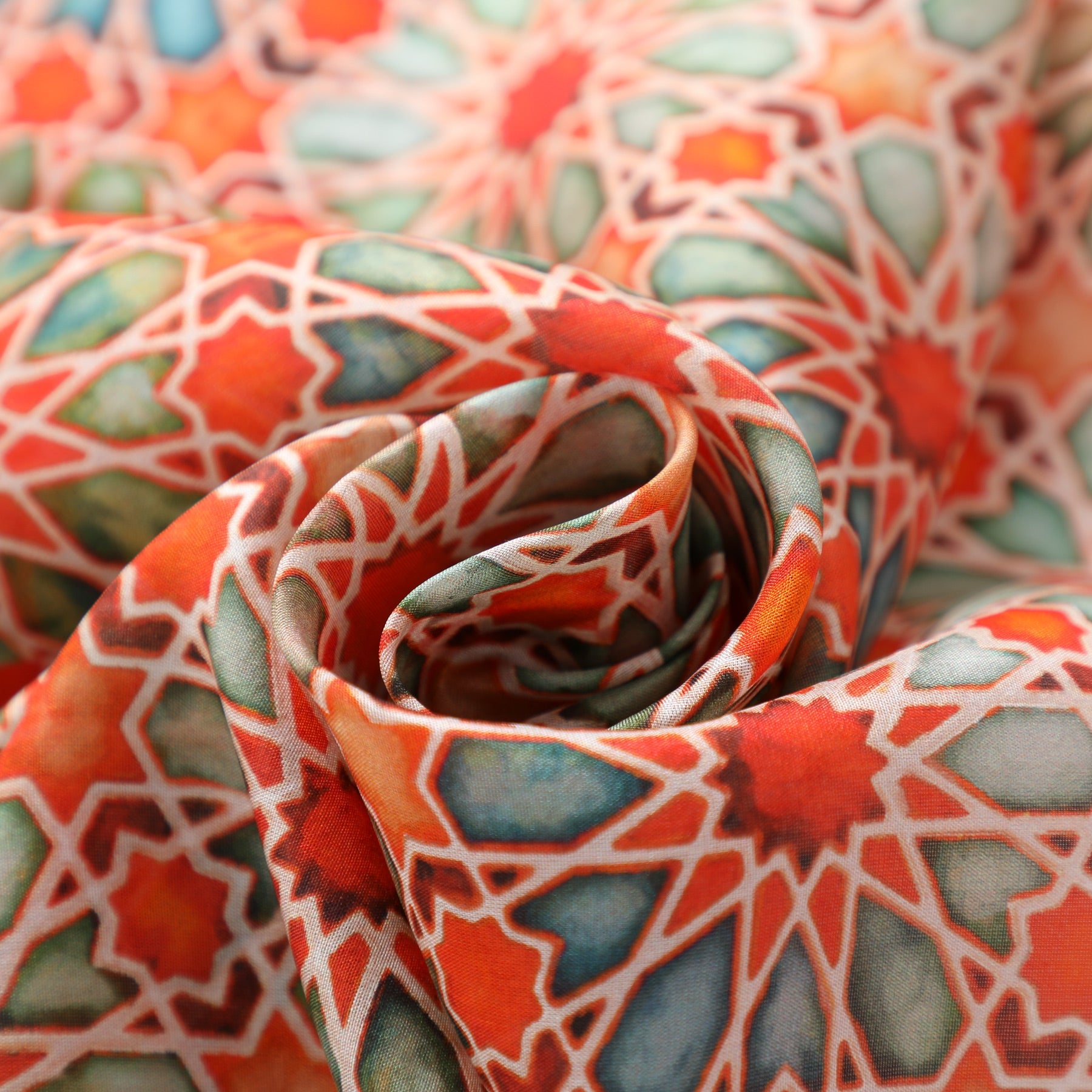 Close-up of the Orange Silk Scarf with Geometric Print Zellige, showcasing its vibrant mosaic-inspired geometric pattern in red, orange, green, and blue. The gentle folds emphasize the scarf’s silky texture and colorful Islamic art motif.