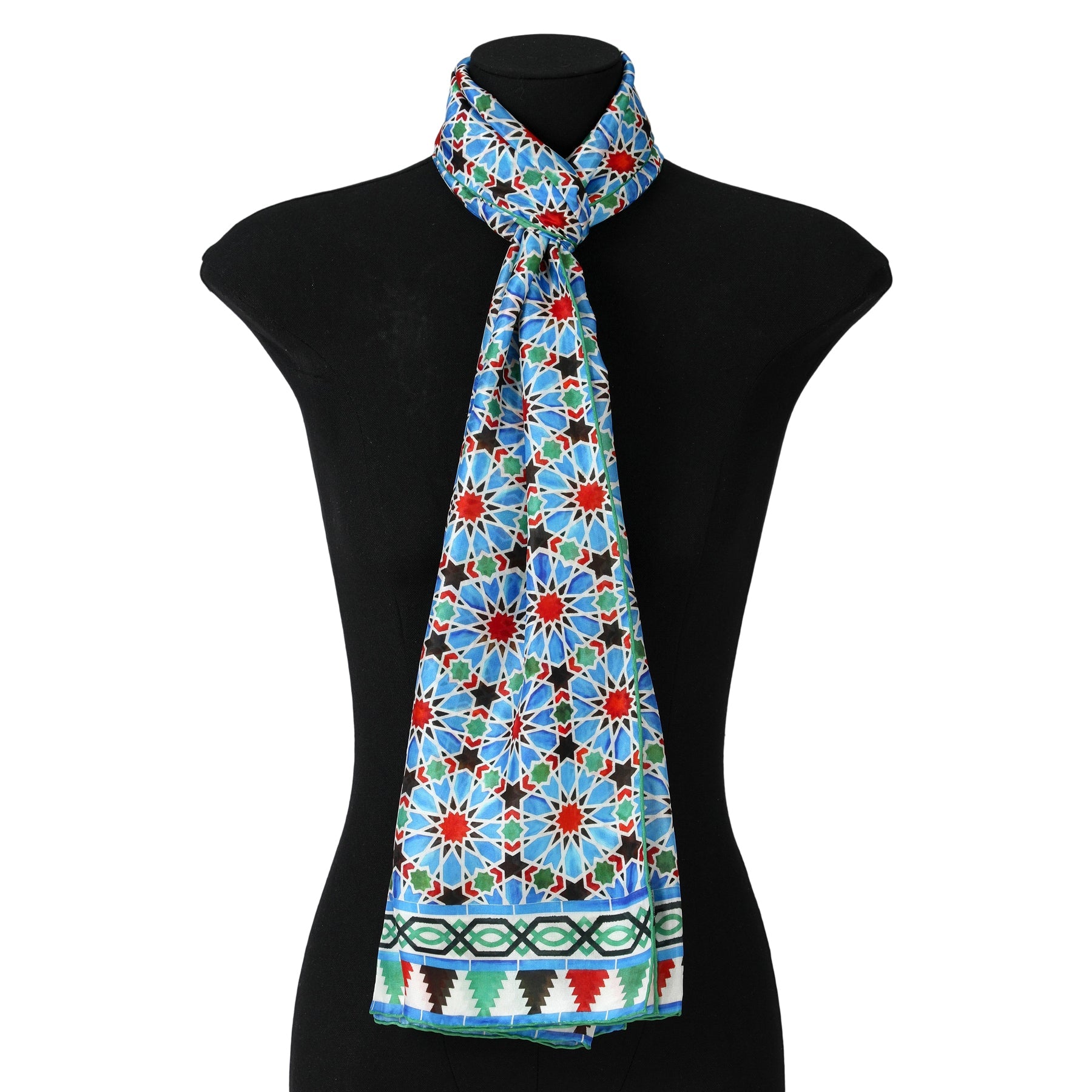 A black mannequin displays the Blue and Red Silk Scarf Zellige, featuring a mosaic-inspired geometric pattern with red, blue, and white shapes and a decorative border. The scarf is tied neatly around the neck for a luxurious touch.