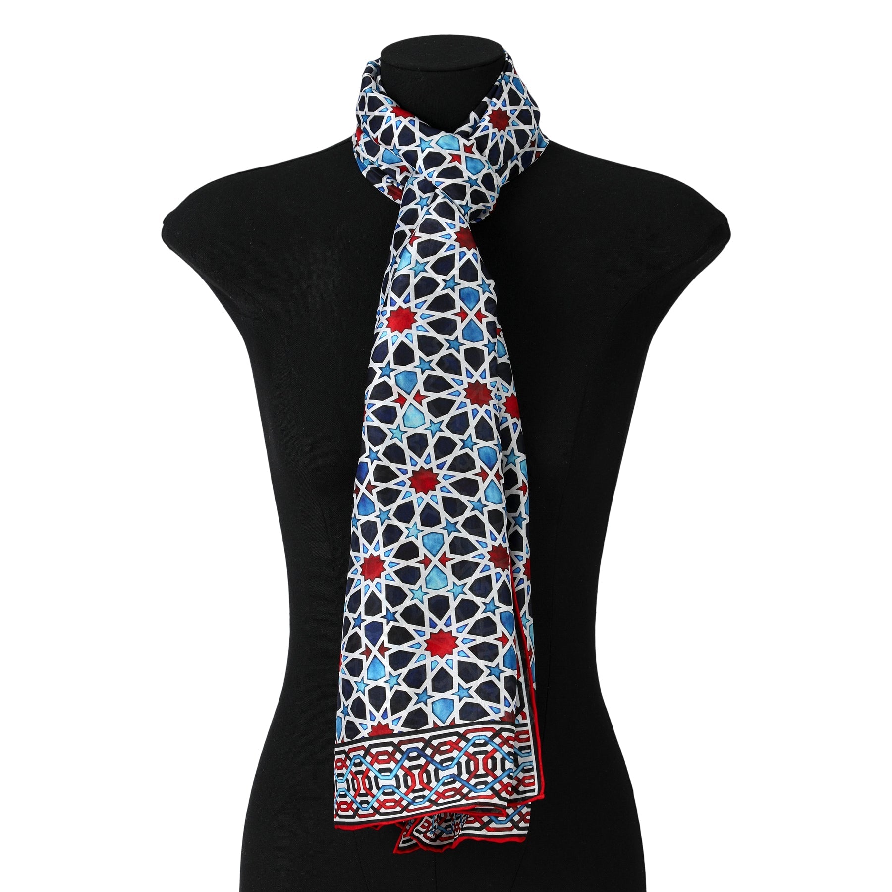 A black mannequin showcases the Alhambra Inspired Silk Scarf Fatima, a long silk accessory with a handmade blue, red, and white mosaic pattern and decorative borders. Neatly tied at the neck, it exudes timeless elegance.
