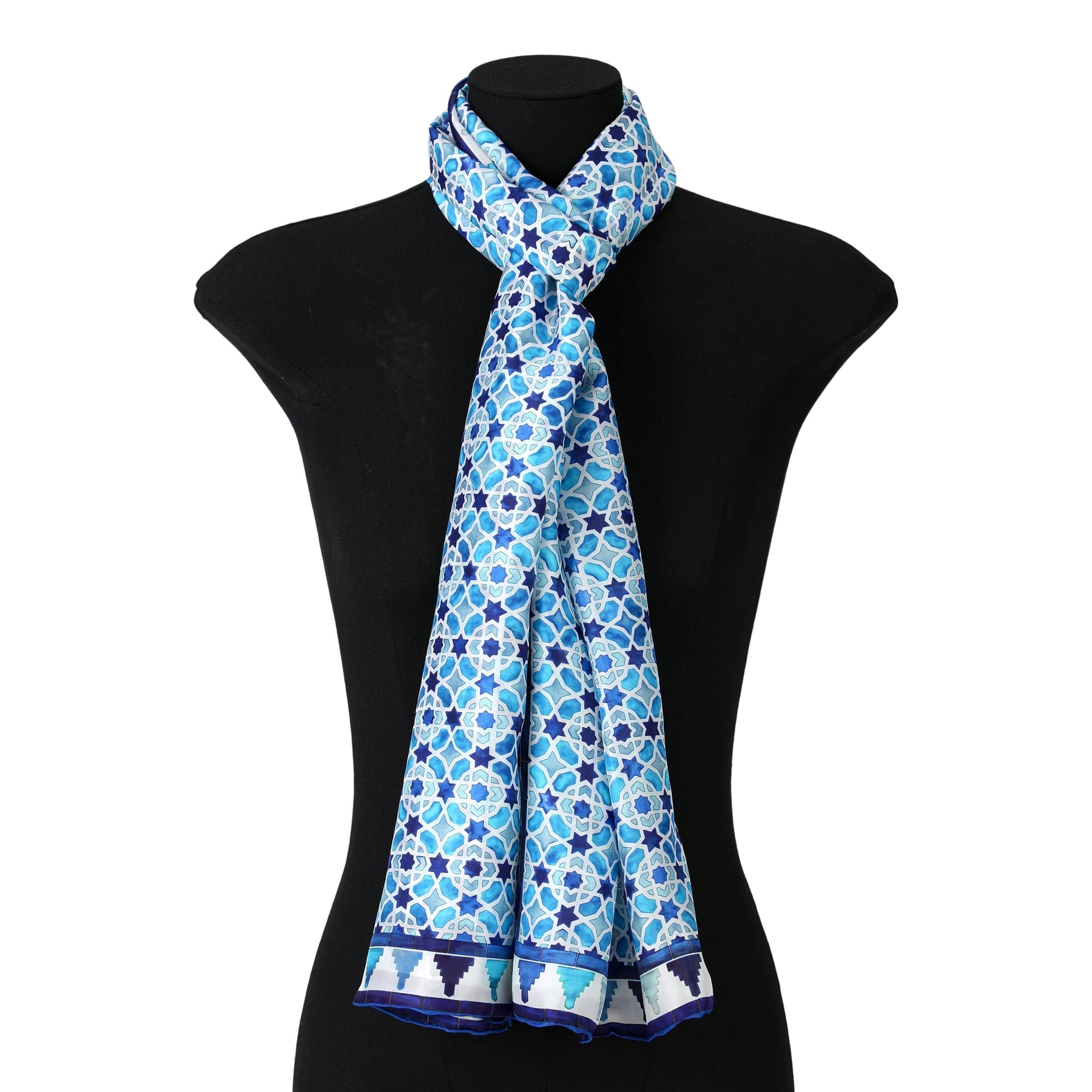 The Light Blue Silk Scarf Alcázar, featuring geometric motifs inspired by Islamic art, is elegantly draped and knotted around the neck of a black dress form mannequin.