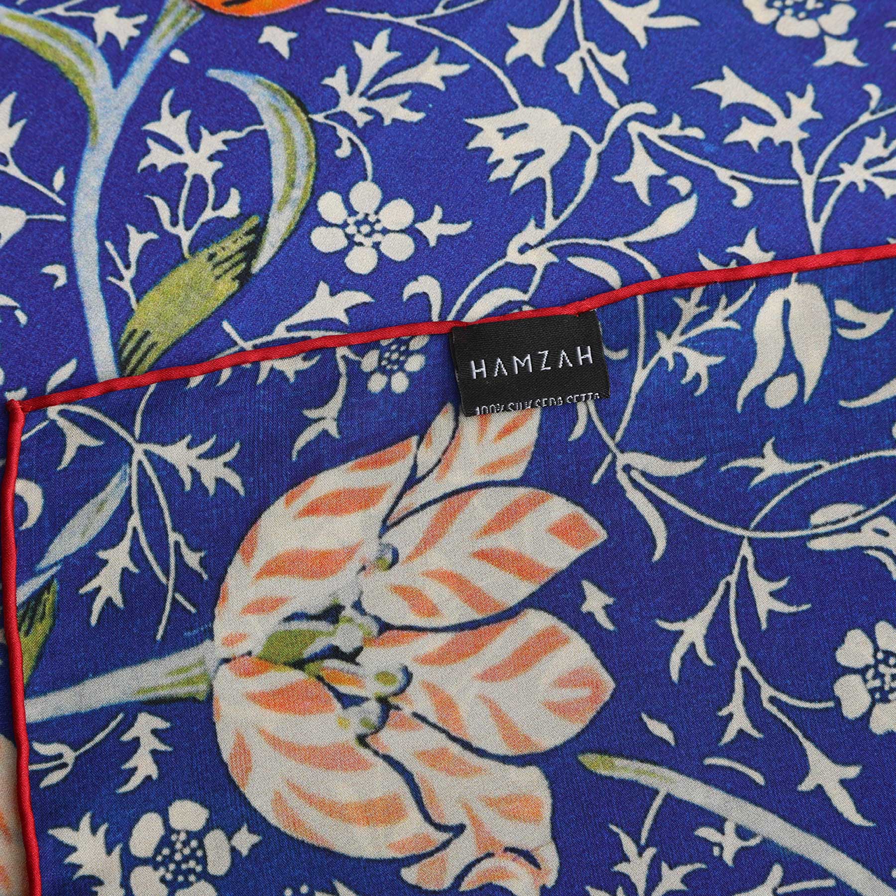 The Floral Blue Silk Scarf Galata, a rectangular blue silk scarf with white floral patterns and a red-orange flower