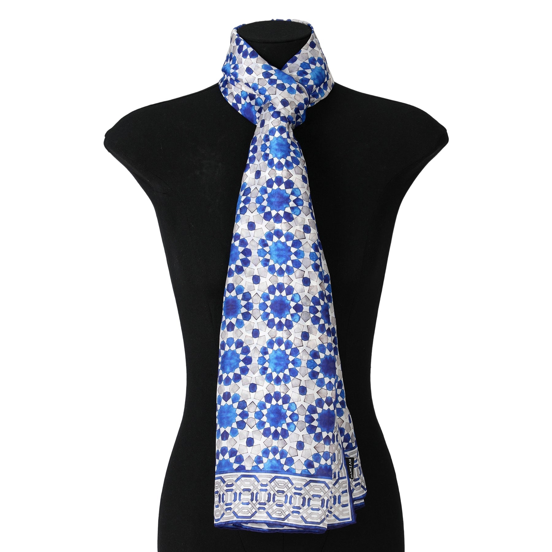 A mannequin showcases the Blue and Grey Silk Scarf Najma, featuring Islamic-inspired geometric patterns, tied simply around the neck for an elegant look.