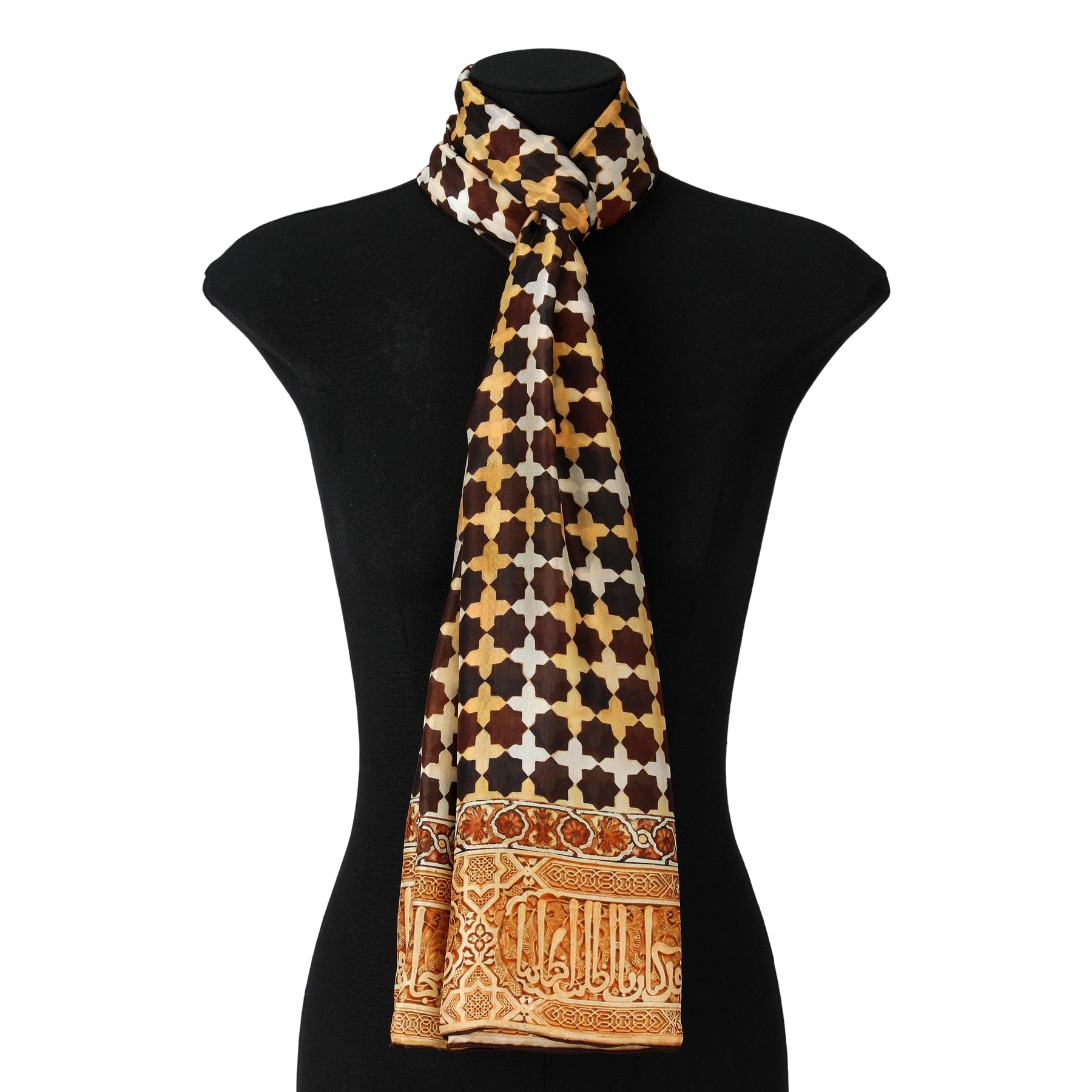 The Brown Large Silk Scarf Andalus features a geometric clover-like pattern in brown, yellow, and white with Moorish-inspired gold and orange motifs and decorative script along the bottom edge. Shown draped on a black dress form.