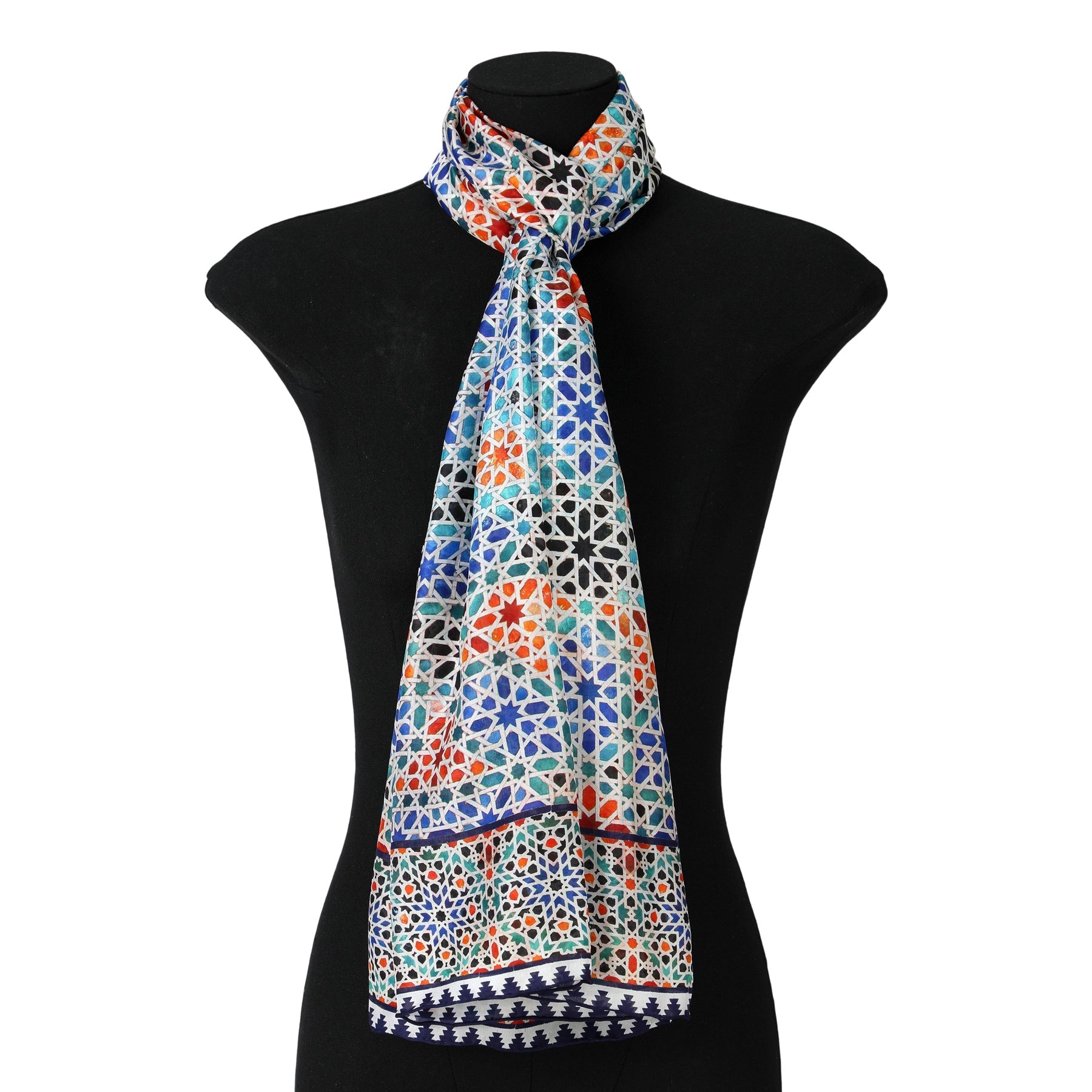 The Multicolored Silk Scarf Madiya, featuring blue, red, and black geometric designs inspired by Islamic art, is draped around a black mannequin torso with the ends hanging down in front.