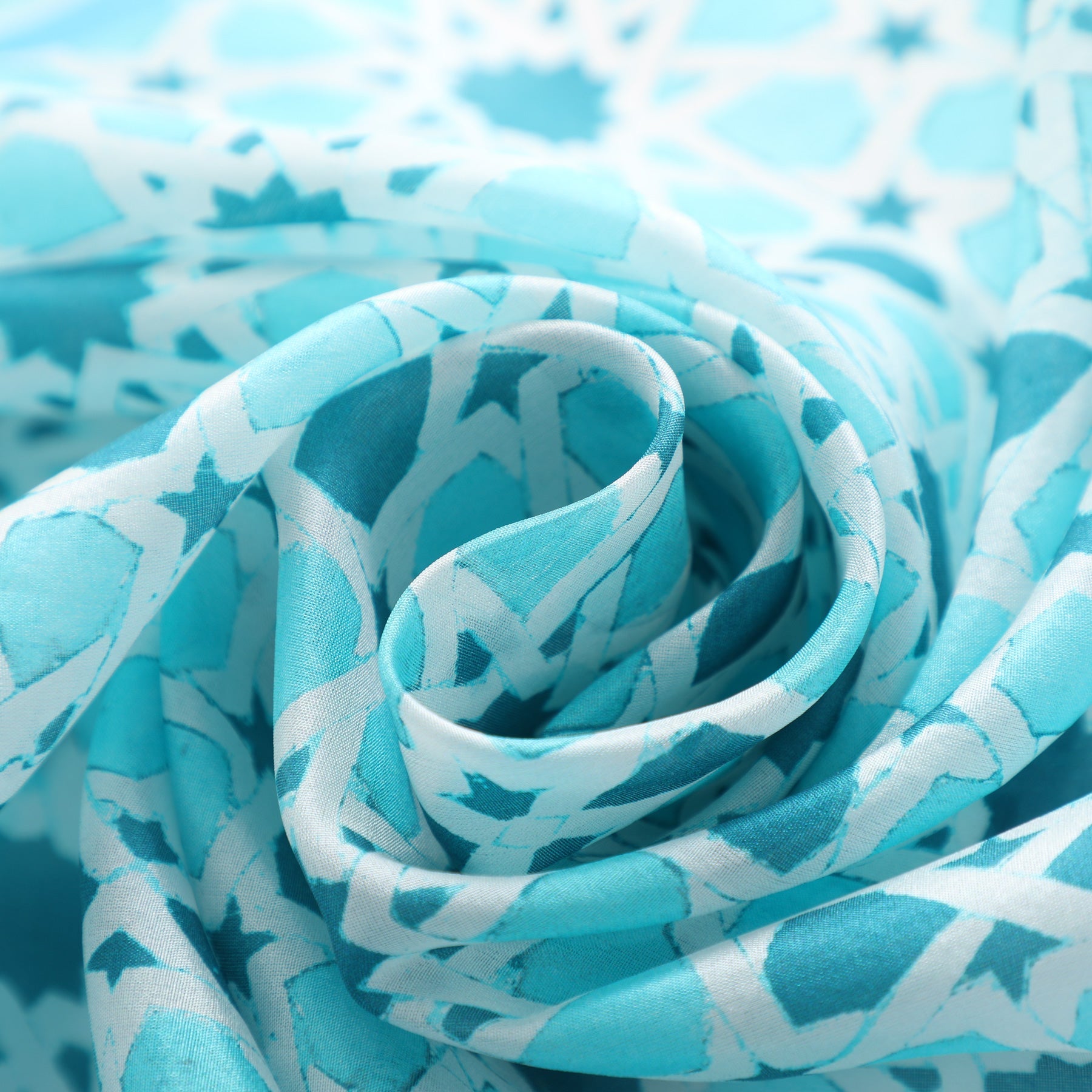 A close-up of the Light Blue Silk Scarf Partal, featuring soft fabric with intricate white and teal geometric designs, artistically arranged in a spiral inspired by Islamic mosaic tiles.