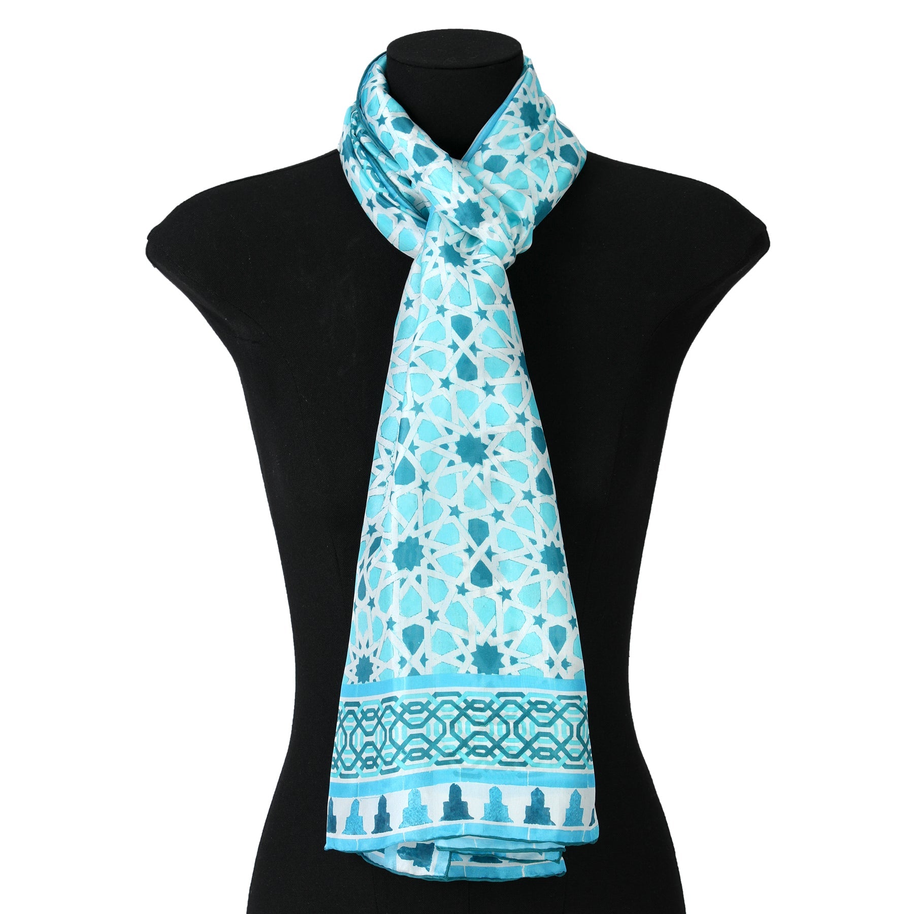 The Light Blue Silk Scarf Partal, featuring a white geometric pattern inspired by Islamic mosaic tiles and a decorative border, is draped around the neck of a black mannequin torso.
