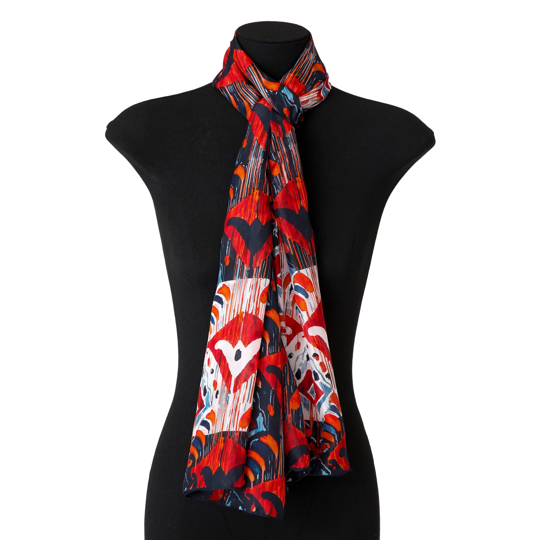 A mannequin displays a long, pleated silk scarf named Red and Blue Silk Scarf with Ikat Print, featuring heart-like and geometric shapes inspired by Indonesian designs, elegantly draped around the neck.