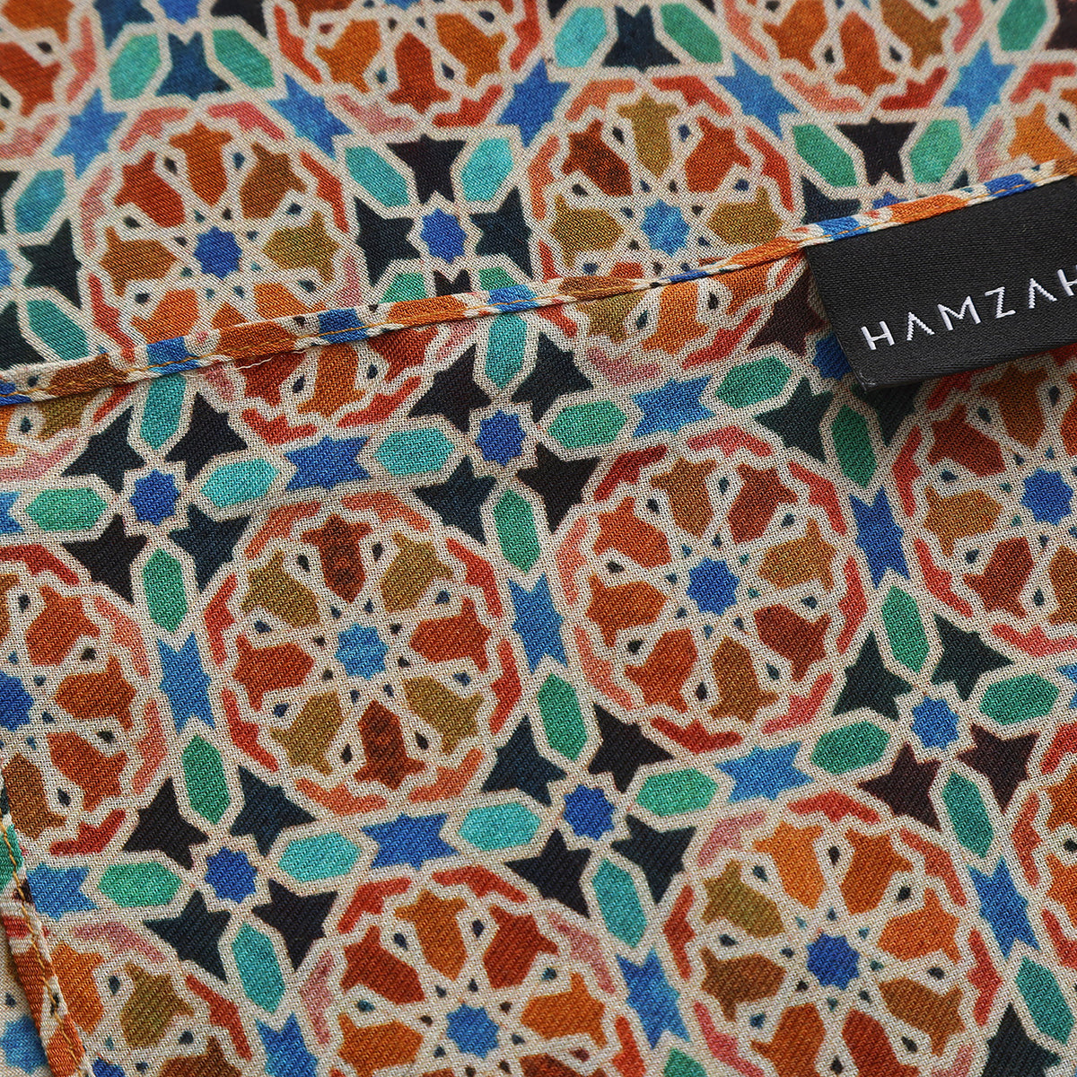 Corner of the Orange Modal Scarf Mosaic Wheels Wallada with the Hamzah woven label
