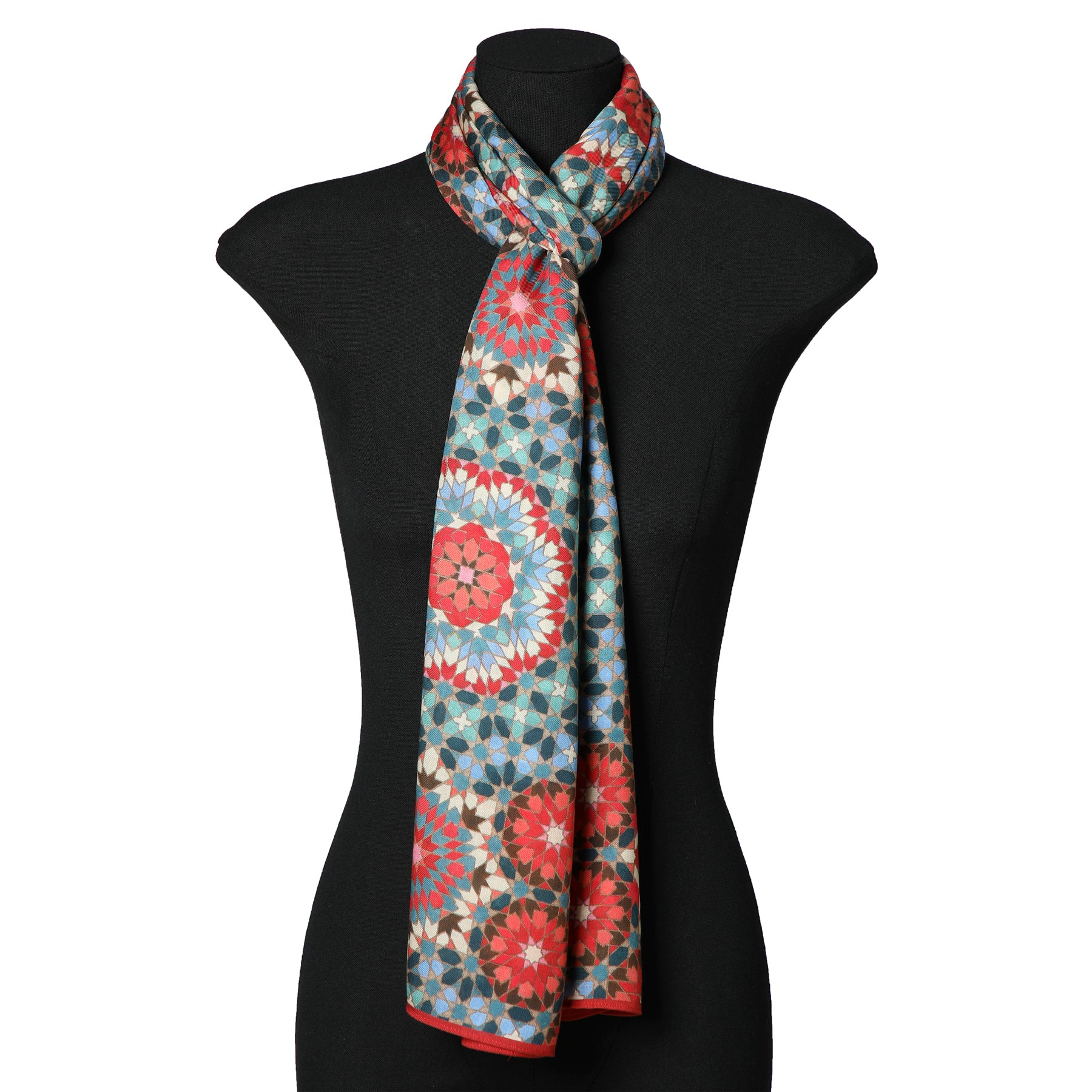 A black mannequin displays the Multicolor Scarf Inspired by Alhambra Tiles, featuring a vibrant geometric floral pattern in red, blue, and white tones, draped around the neck and hanging down the front.
