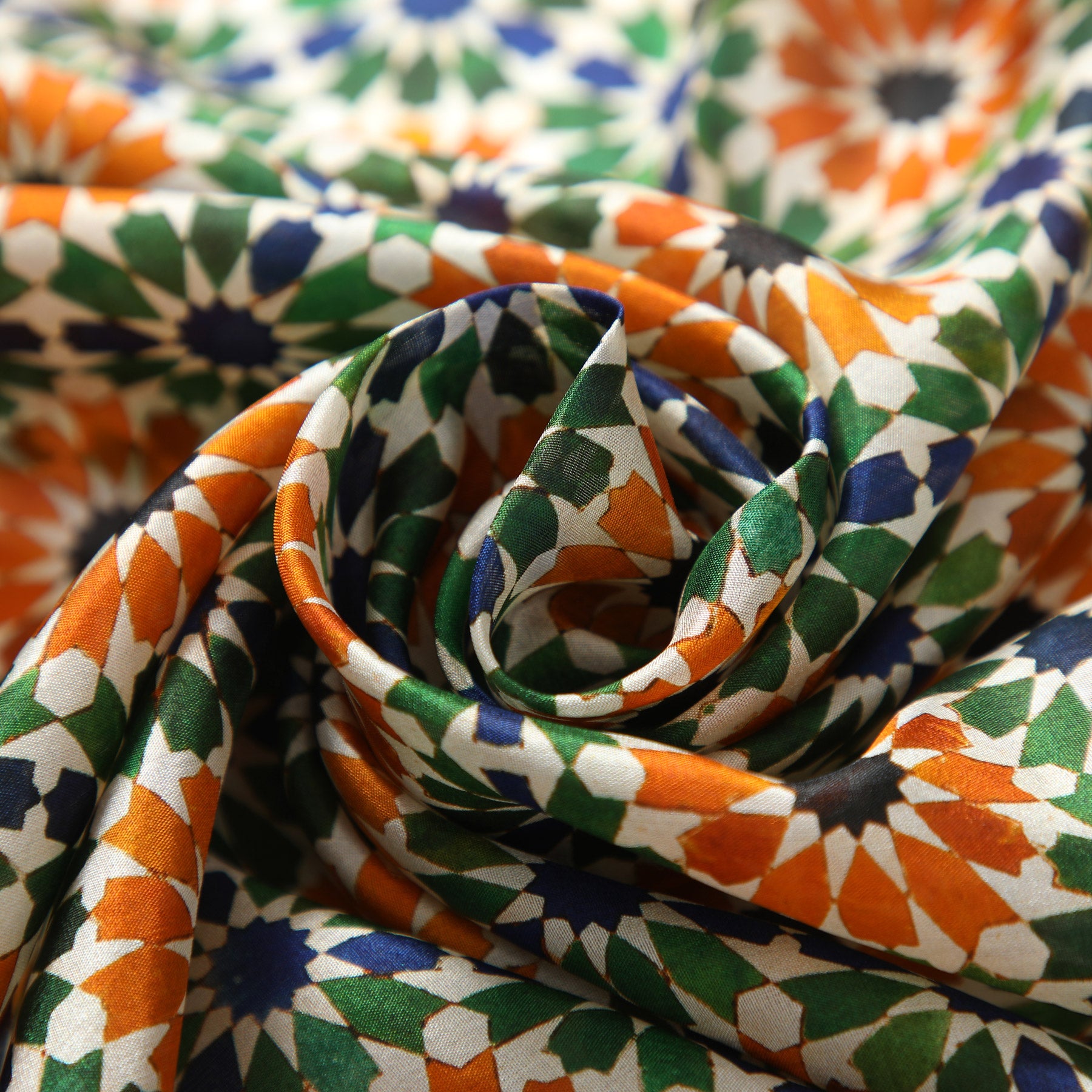 Close-up of the Nur silk print: eight-pointed stars in orange, bottle green and navy on cream