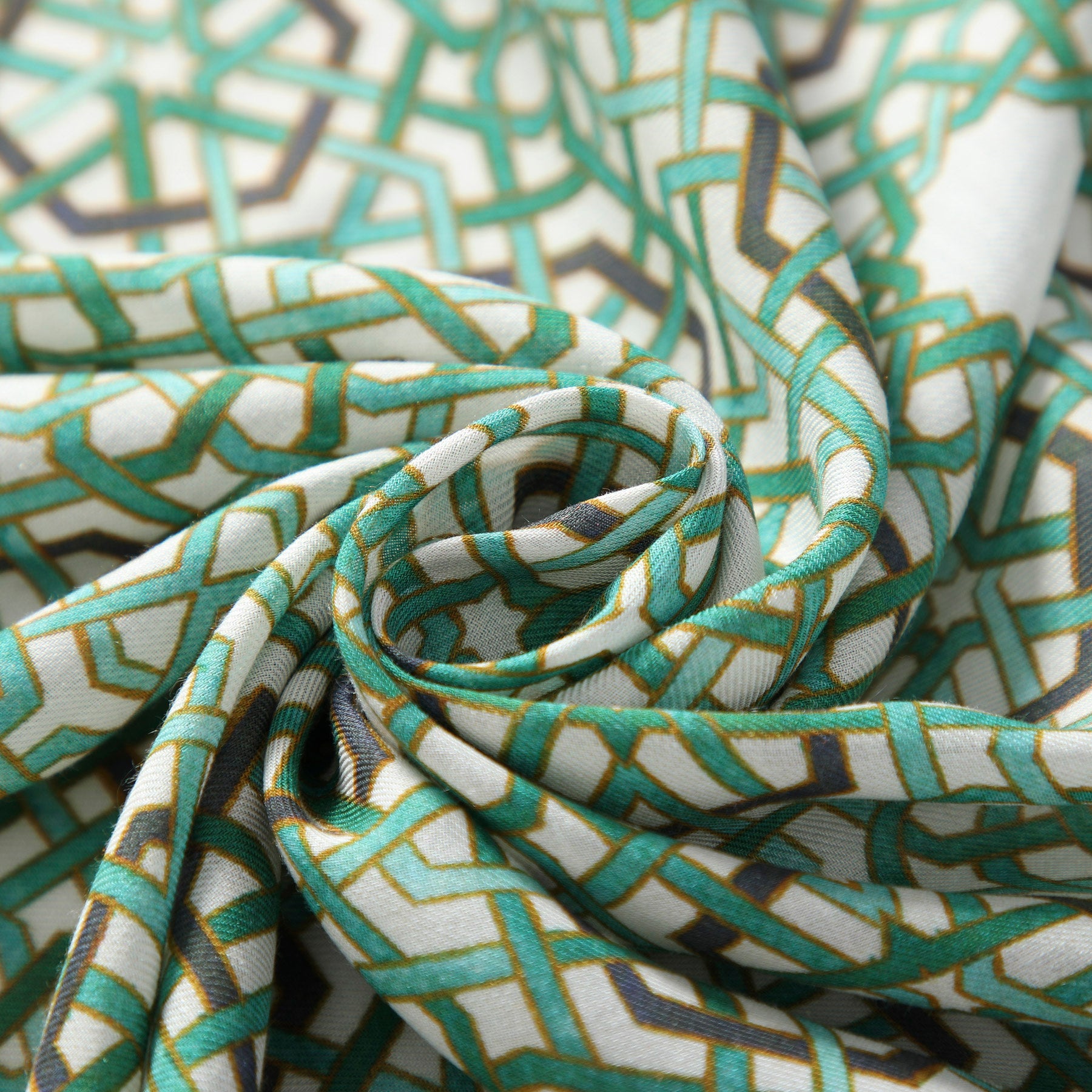 A close-up of the Modal Hijab with Green Geometric Print, featuring gold and white Islamic-inspired patterns. The fabric is loosely twisted to showcase its smooth texture and intricate design—an ideal choice for a stylish hijab.