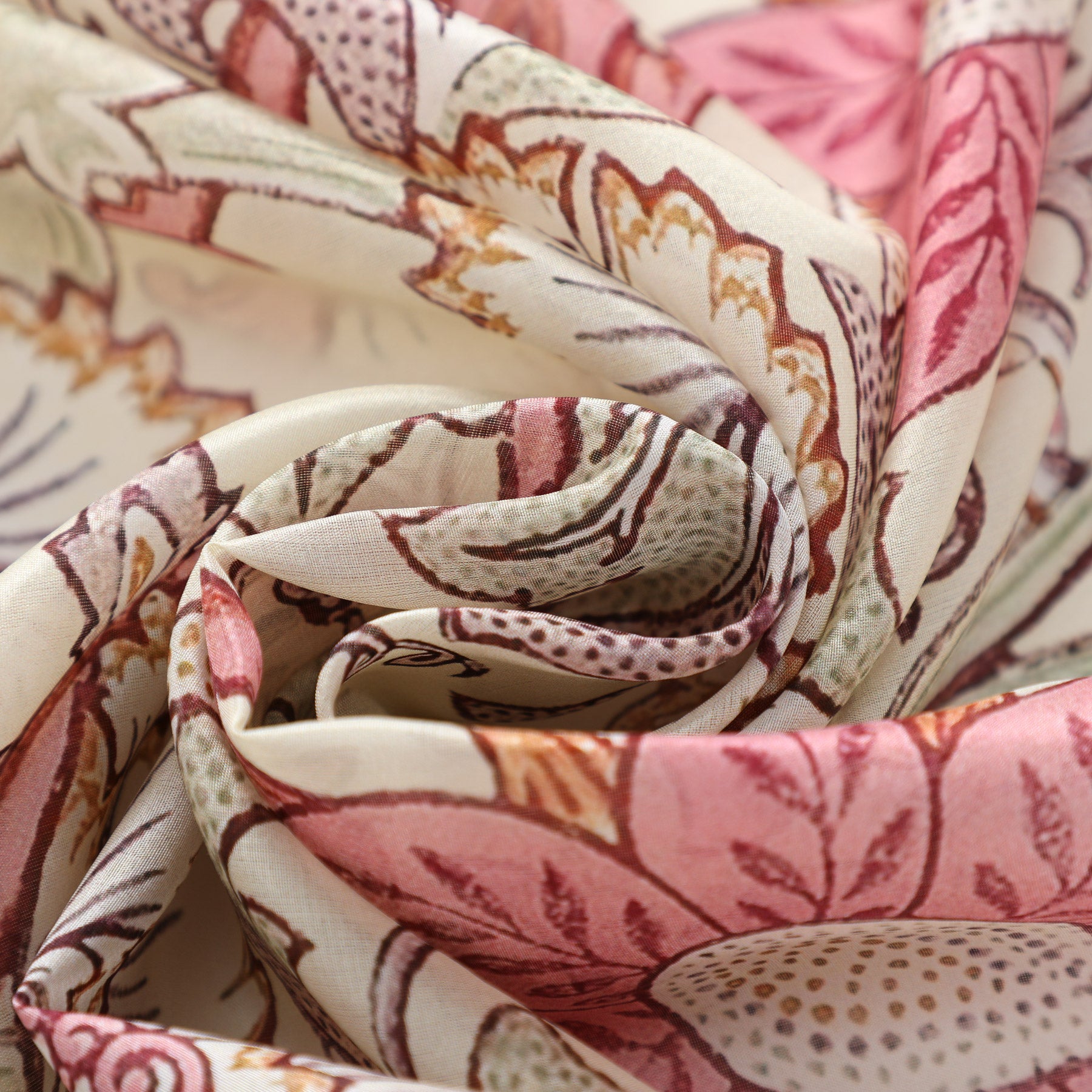A close-up of the W. Morris Art Nouveau Scarf by Hamzah showcases its floral pattern in soft pink, beige, and brown tones. Intricately folded into a swirling rose-like shape, the 100% Habotai silk scarf highlights its detailed design and delicate texture.