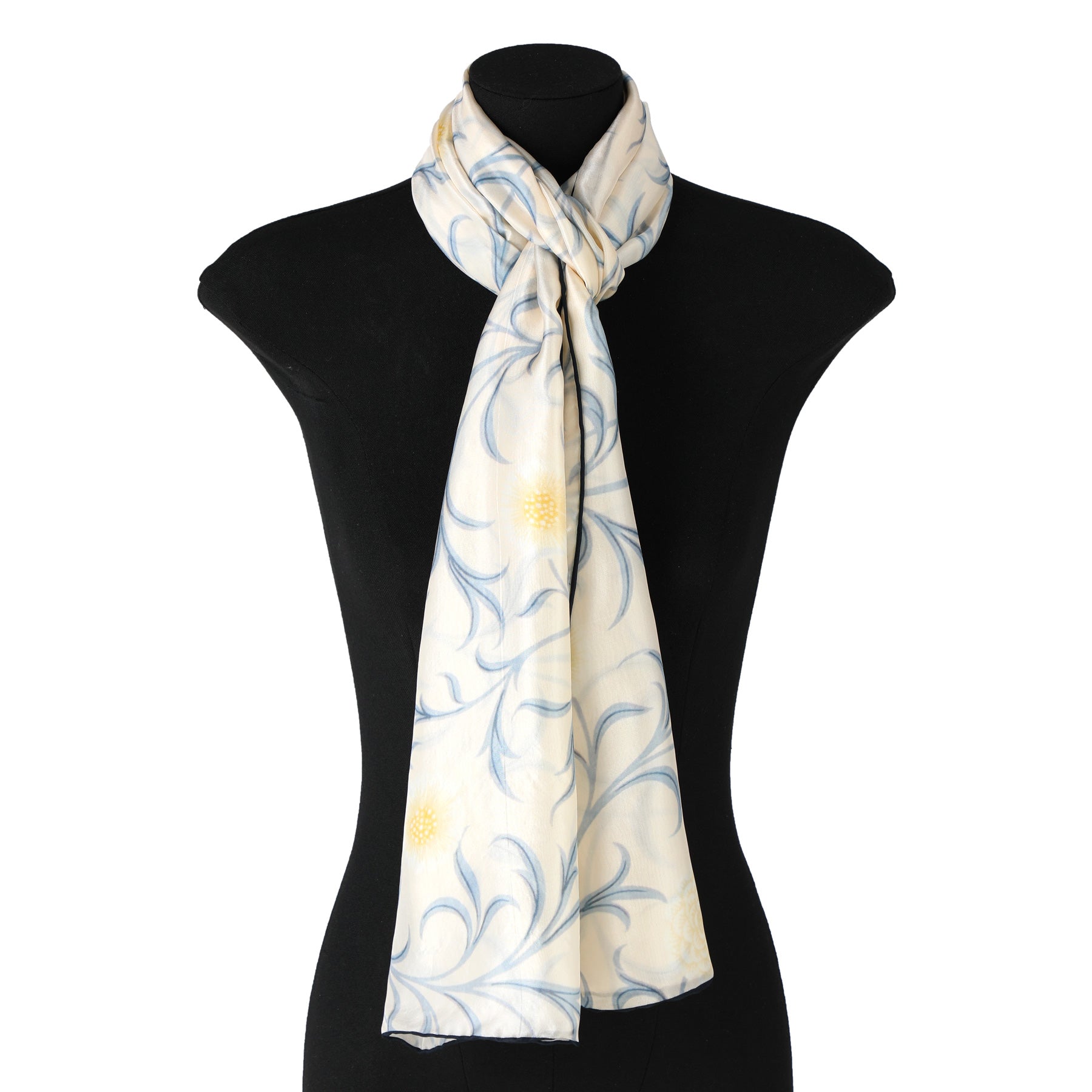 A mannequin displays the Hamzah William Morris Floral Scarf in cream-colored Habotai silk, adorned with a blue and yellow floral design, elegantly knotted around its neck against a plain white background, adding sophistication to any ensemble.