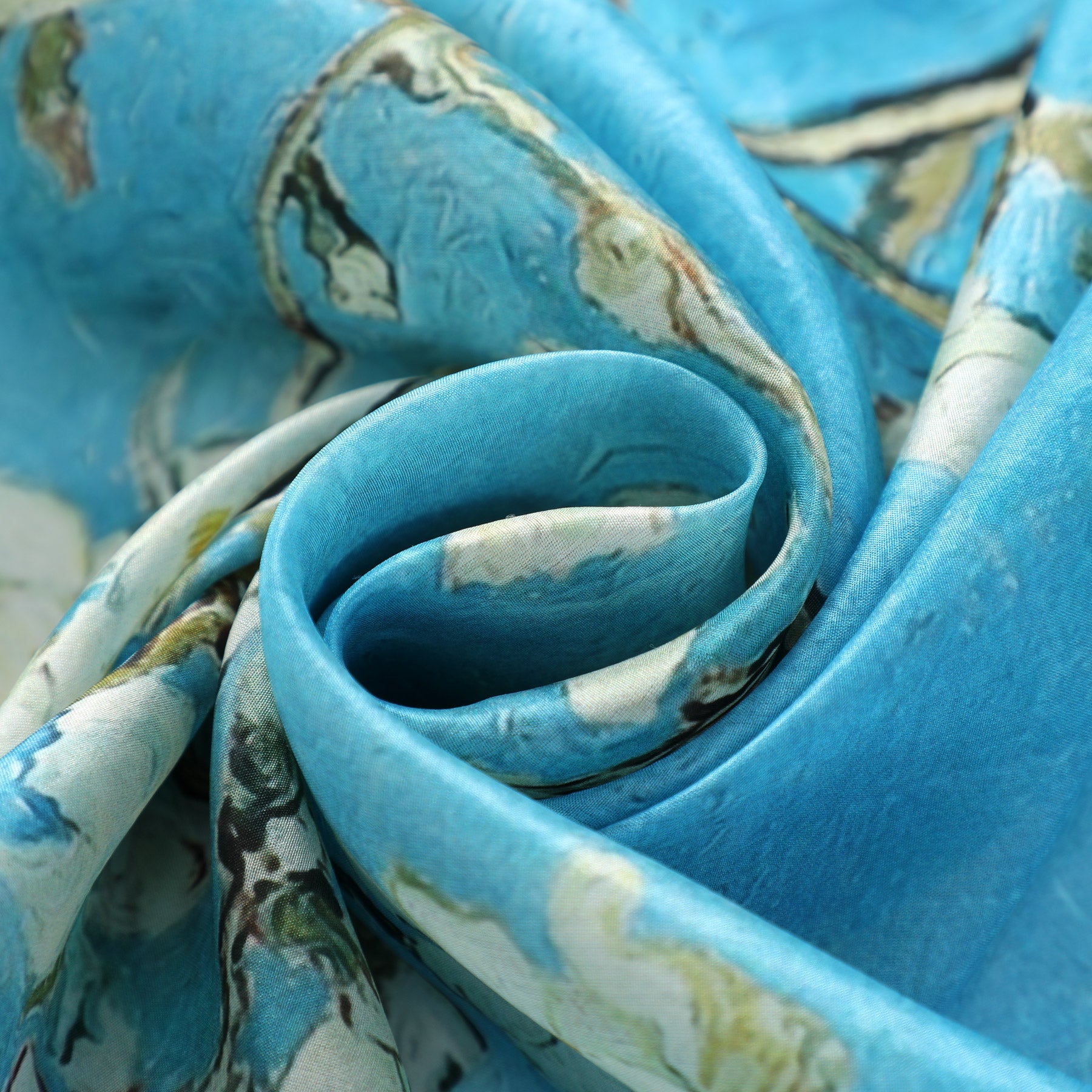 The Van Gogh Silk Scarf - Amandelbloesem by Hamzah features a close-up of a swirling pattern in blue and green hues. Crafted from smooth Habotai silk, its folded into a spiral to highlight its intricate design.