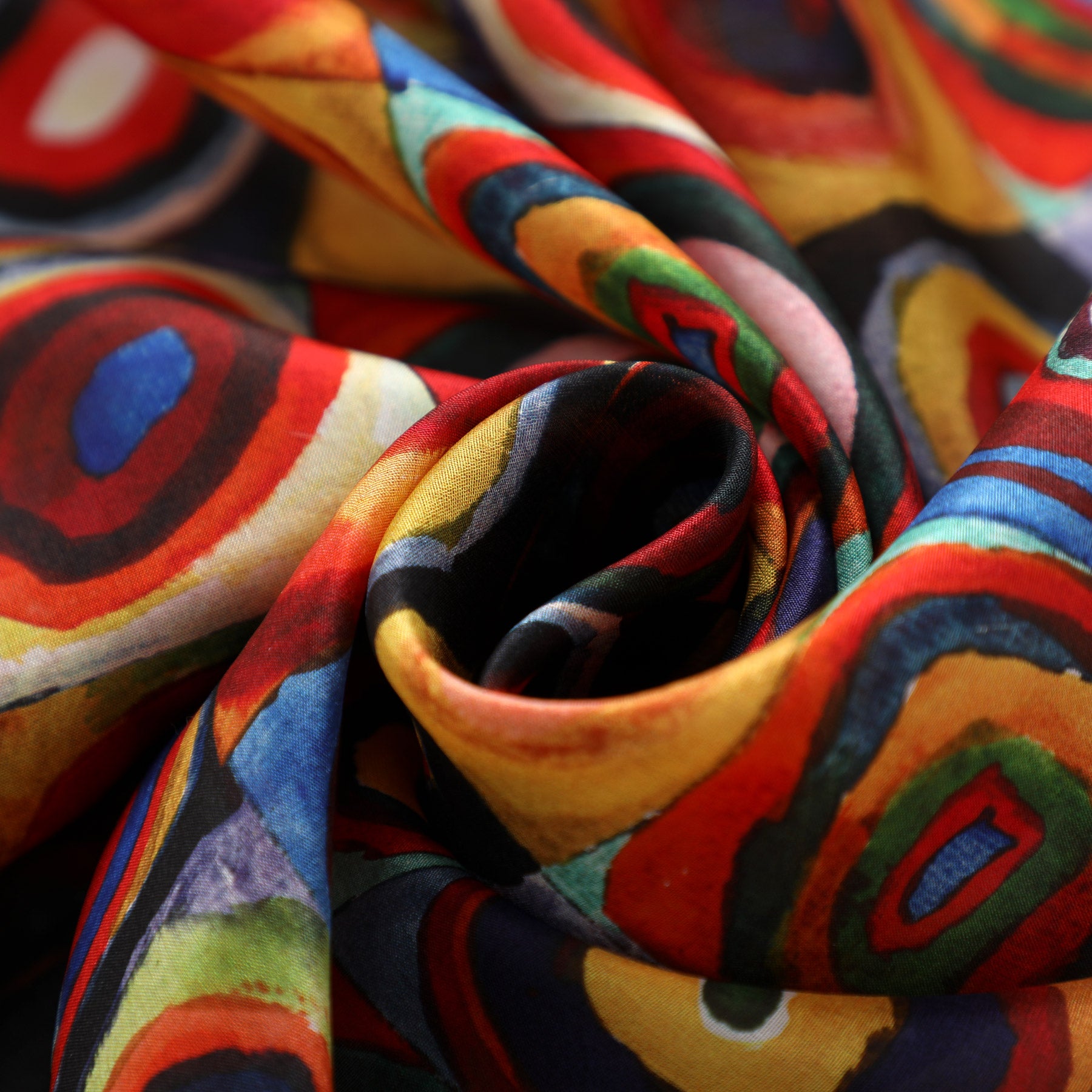 Close-up of the vibrant Hamzah Kandinsky Scarf, made of 100% silk, showcasing swirling abstract patterns in red, blue, orange, and green. The softly folded fabric exudes movement and texture reminiscent of a Color Study print.