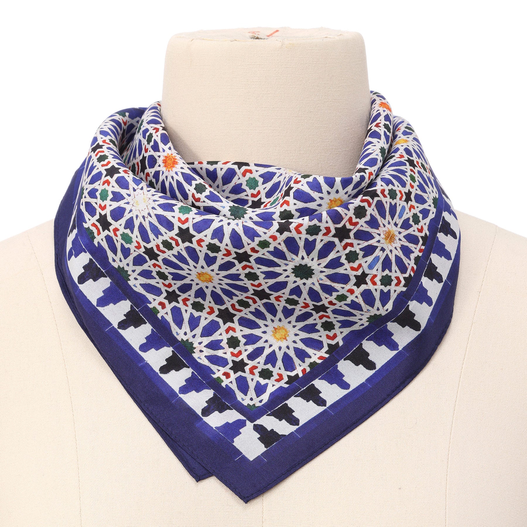 A mannequin showcases the Blue Square Scarf Zellige v2, featuring a blue and white geometric pattern inspired by Islamic art, accented with multicolors and stylishly draped around the neck.