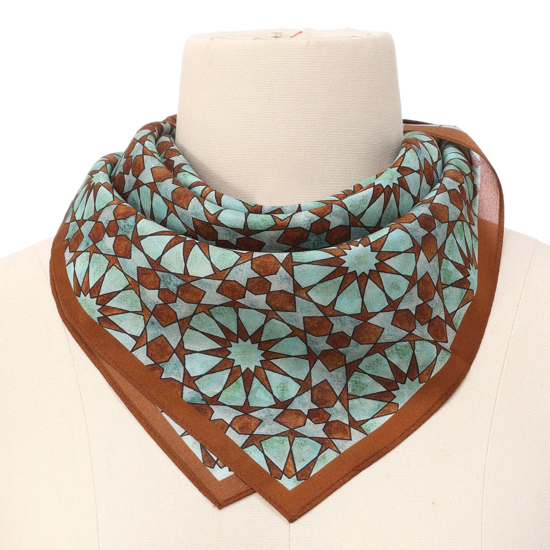 The Brown Silk Neckerchief for Women, featuring an Islamic art print, drapes elegantly on the mannequin and highlights exquisite Spanish craftsmanship.