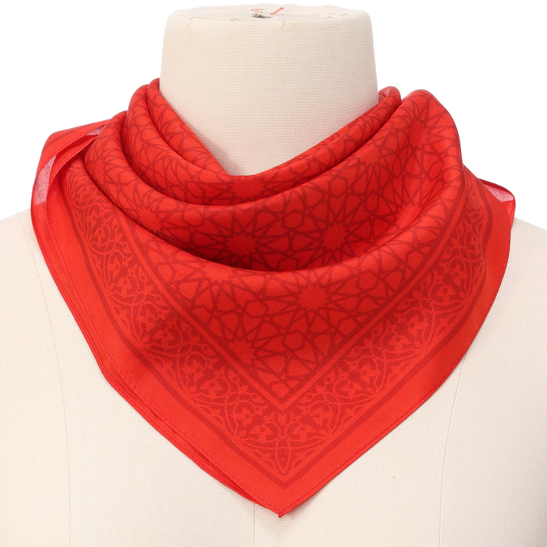 The Red Square Scarf Dalila v2, crafted from 100% silk and featuring intricate Islamic-inspired geometric designs, is stylishly draped around the neck of a white mannequin bust.