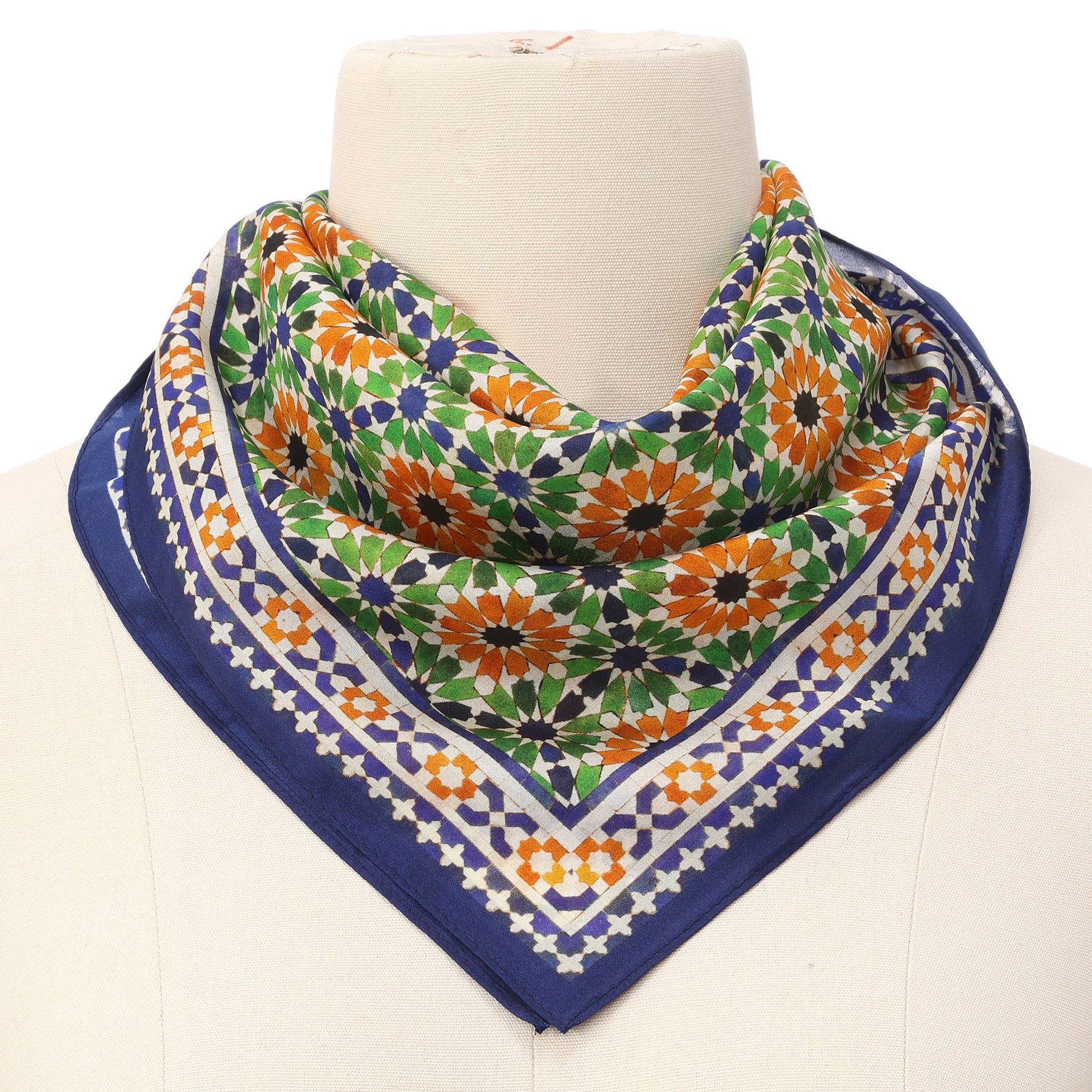 A mannequin showcases the Islamic Art Print Square Silk Scarf Nur, featuring a colorful geometric floral pattern in green, orange, and blue with a navy blue border and motifs inspired by Islamic art.