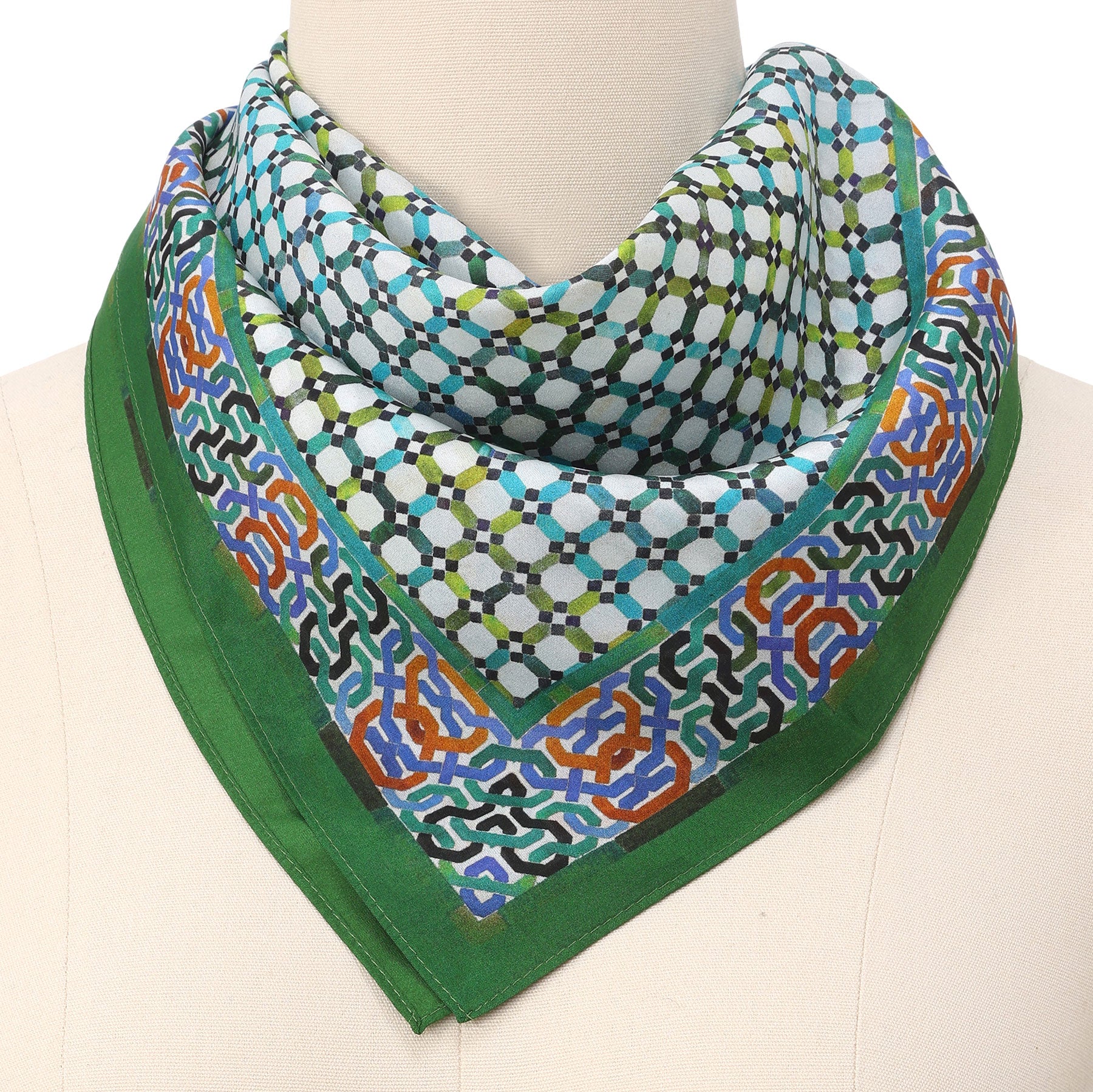 A mannequin showcases the Coloful Neckerchief 100% Silk, featuring an Islamic art-inspired geometric pattern in blue, white, green, and black with a bold green border and intricate orange-blue edge details, elegantly draped around the neck.