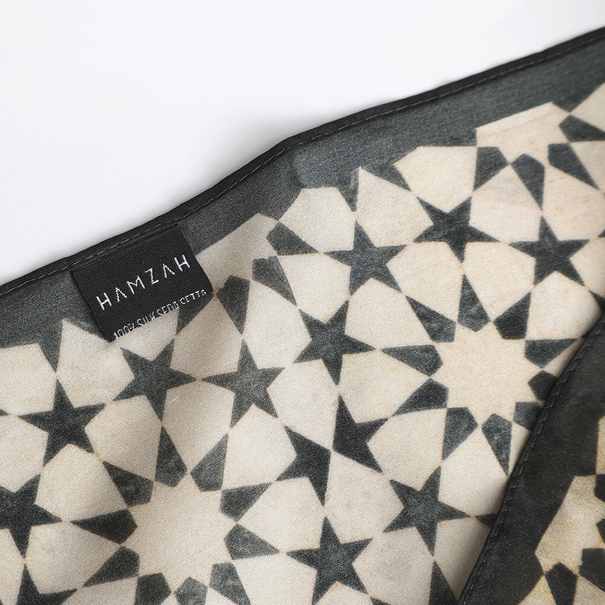Corner of the Black and Cream Silk Square Scarf Nujum with the Hamzah woven label