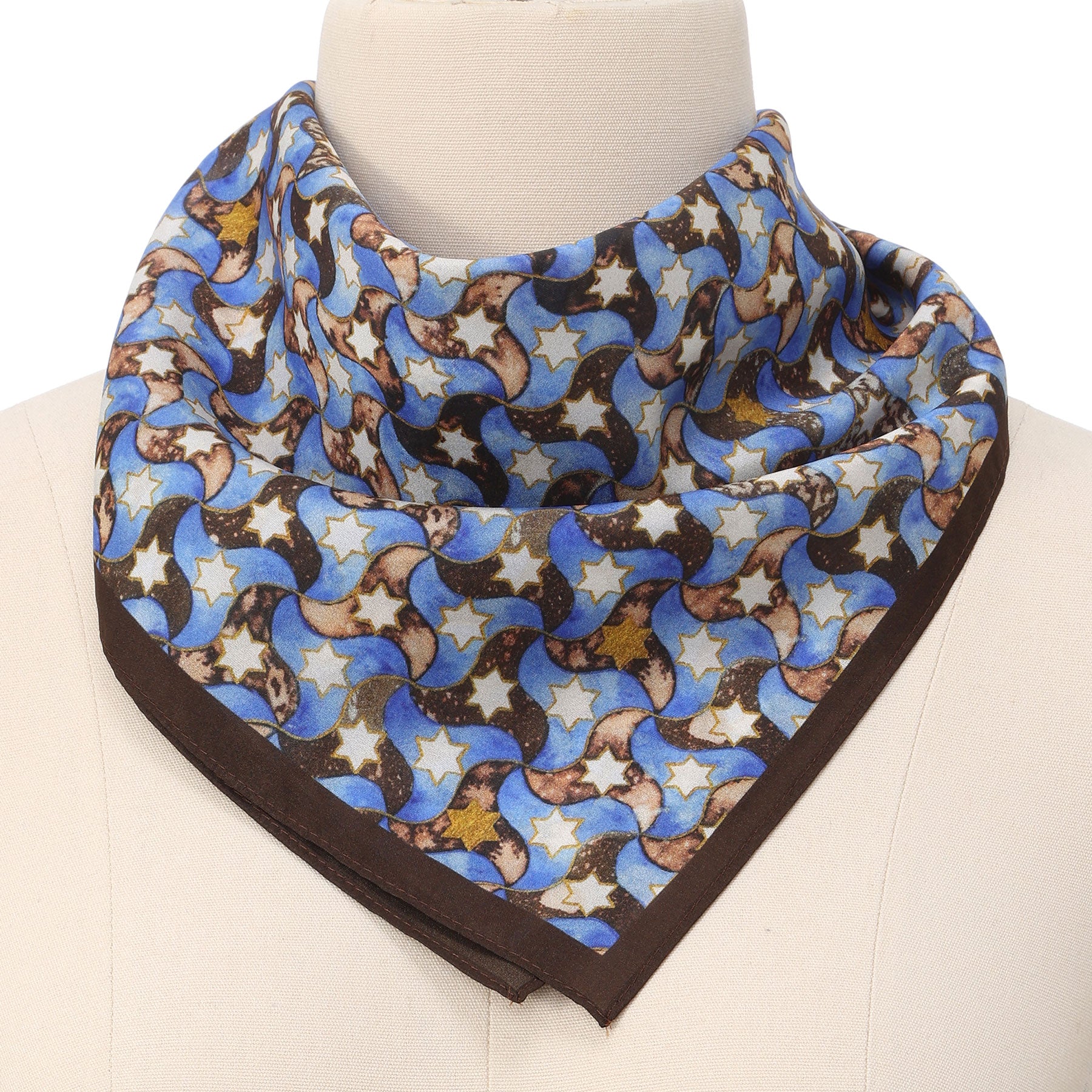 A mannequin displays the Silk Square Scarf for Women Brown, featuring a light blue base with celestial motifs—blue crescent moons, tan stars, and brown accents—framed by a dark brown border inspired by Islamic art.