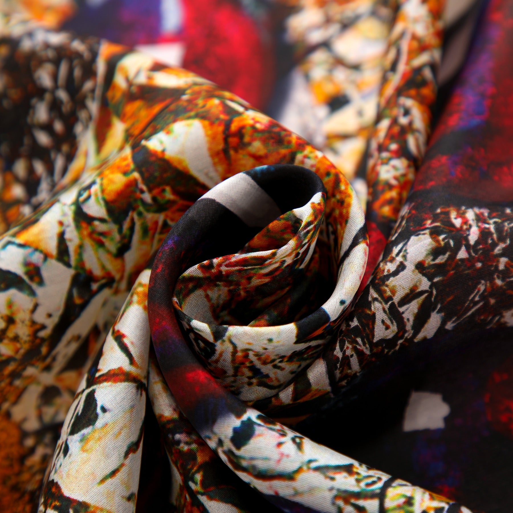 A close-up of the Habotai Silk Scarf Corazón de Granada displays vibrant, multicolored abstract patterns—orange, yellow