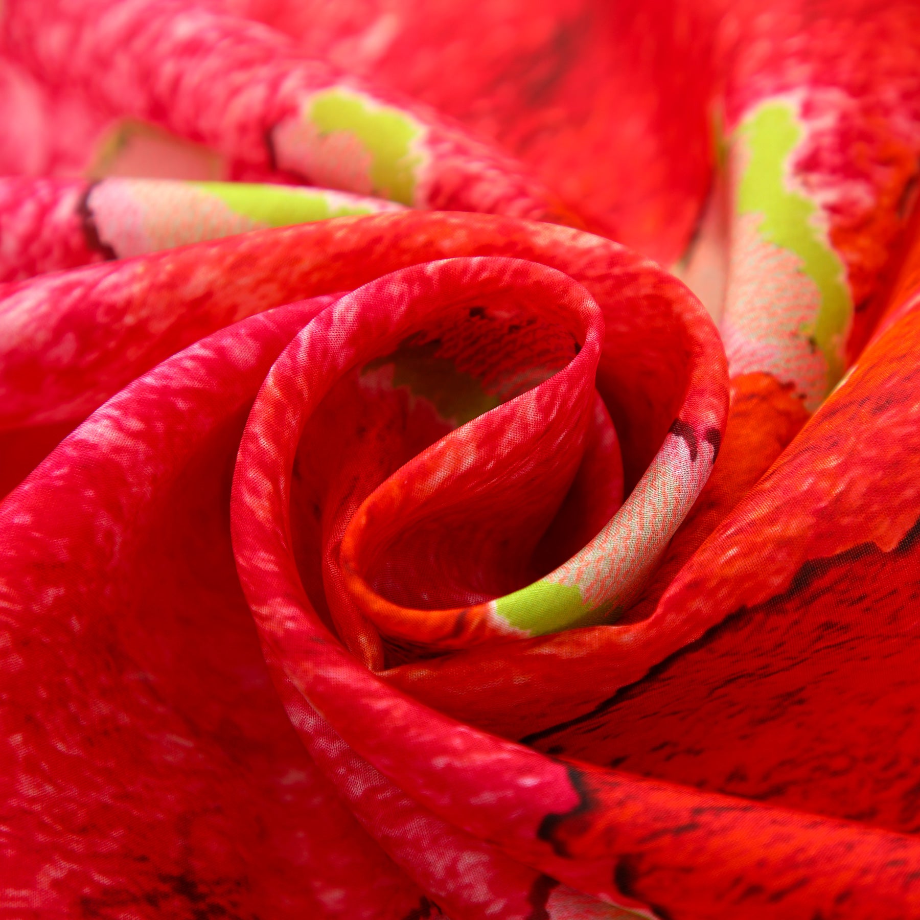 A close-up of the Fuchsia Silk Scarf for Women, featuring vibrant red and pink hues with touches of green and white, artfully folded to highlight its soft, textured habotai silk and vivid colors.