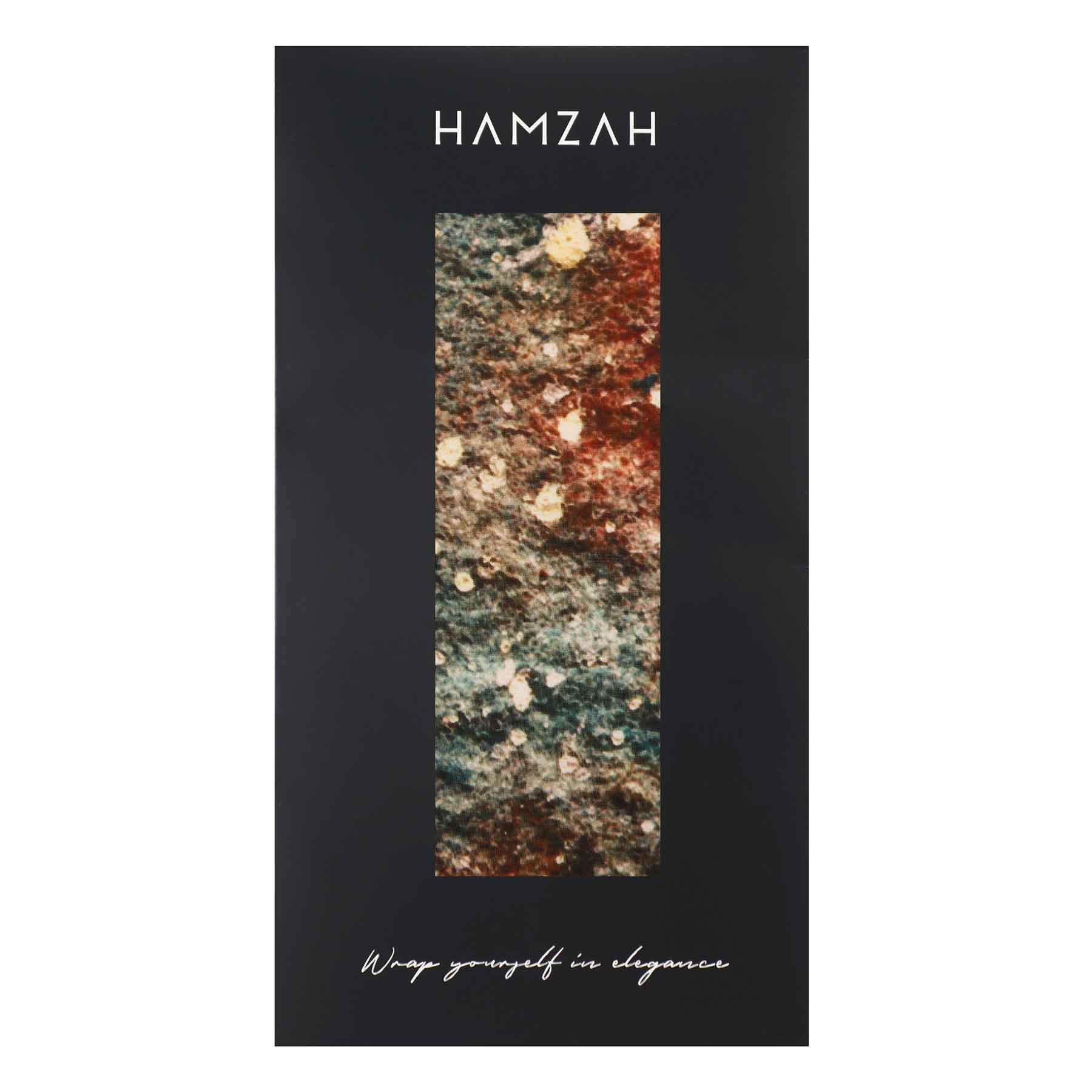 A black rectangular box with HAMZAH at the top, a vertical window showing the multicolored Silk Foulard for Men Polvo Cósmico scarf inside, and "Wrap yourself in elegance" at the bottom—a distinctive Mediterranean accessory.