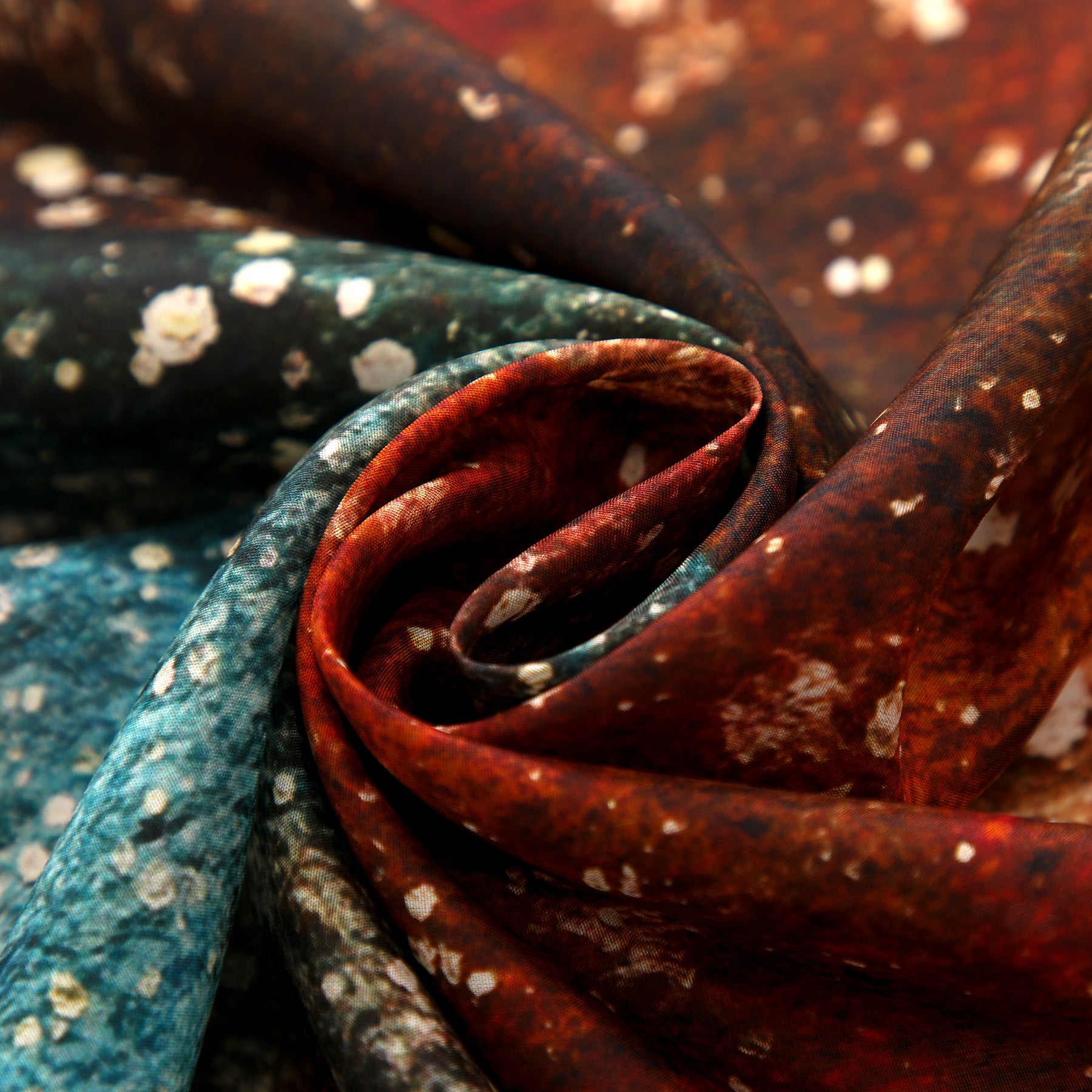 A close-up of the Silk Foulard for Men Polvo Cósmico, featuring a marbled pattern in red, green, and white tones, twisted to showcase its lustrous texture—an elegant Mediterranean-inspired accessory.