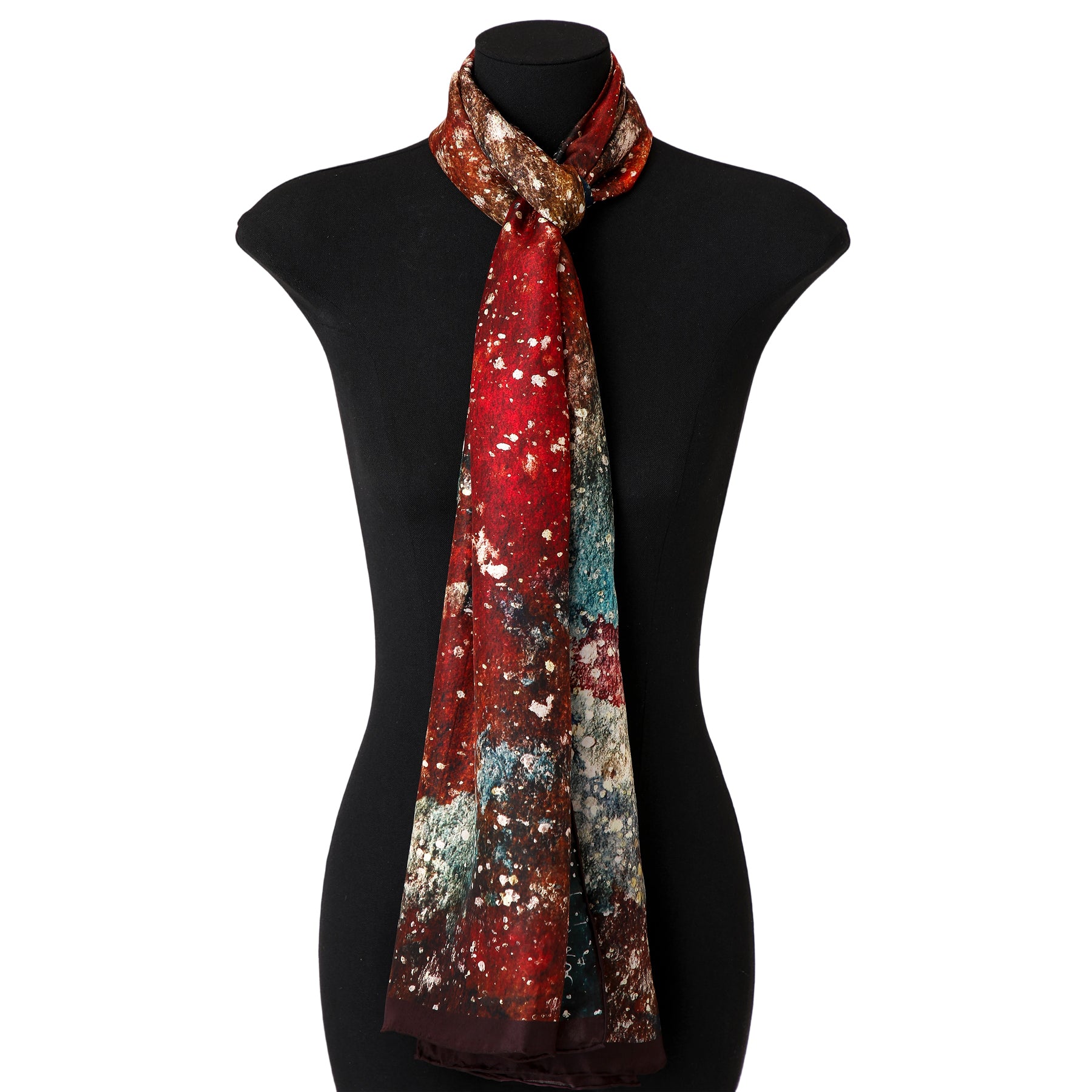 A mannequin showcases the Silk Foulard for Men Polvo Cósmico, a long habotai silk scarf with an abstract design in red, brown, white, and teal, tied loosely around the neck and draping down the front.